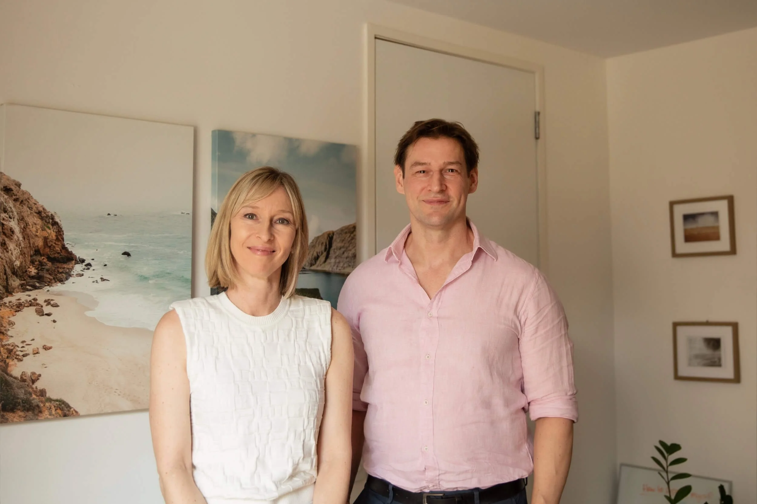 Dr Matt Evans & Natalie Evans standing side by side in a room with beach-themed artwork on the wall.