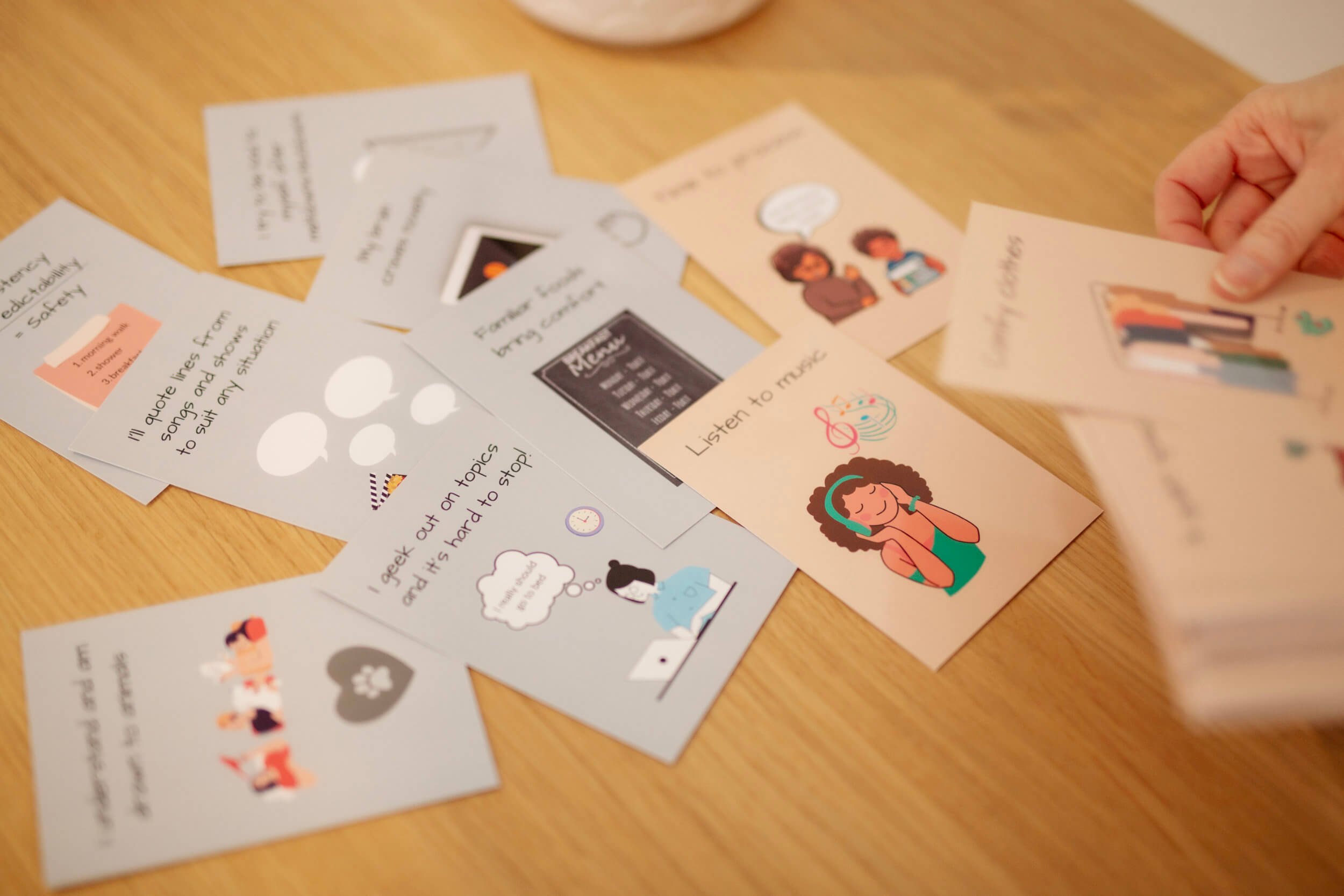 Various educational and informational illustrated cards and sheets spread out on a wooden surface. A person's hand is holding one of the cards.