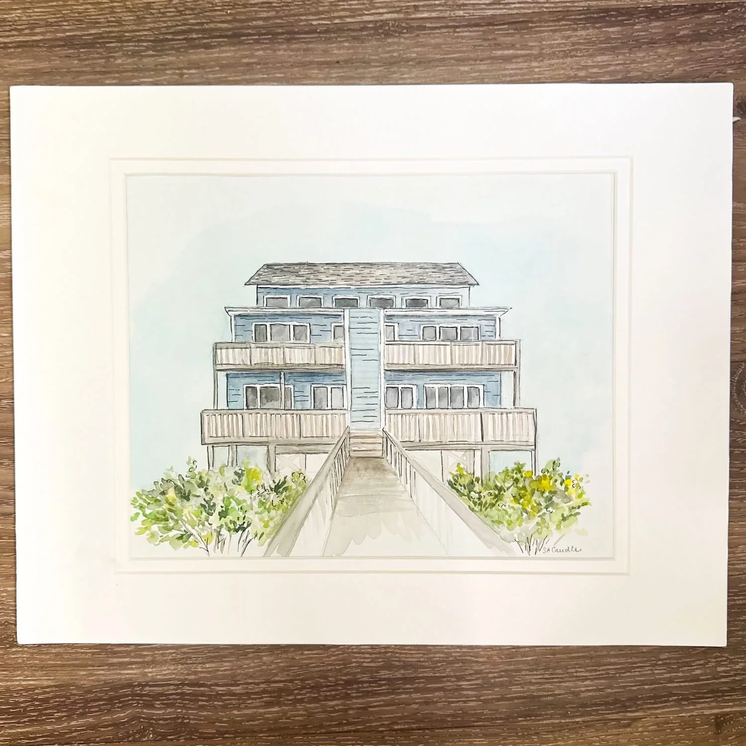 Watercolor painting of a multi-story building with balconies, seen from a pathway with bushes on either side.