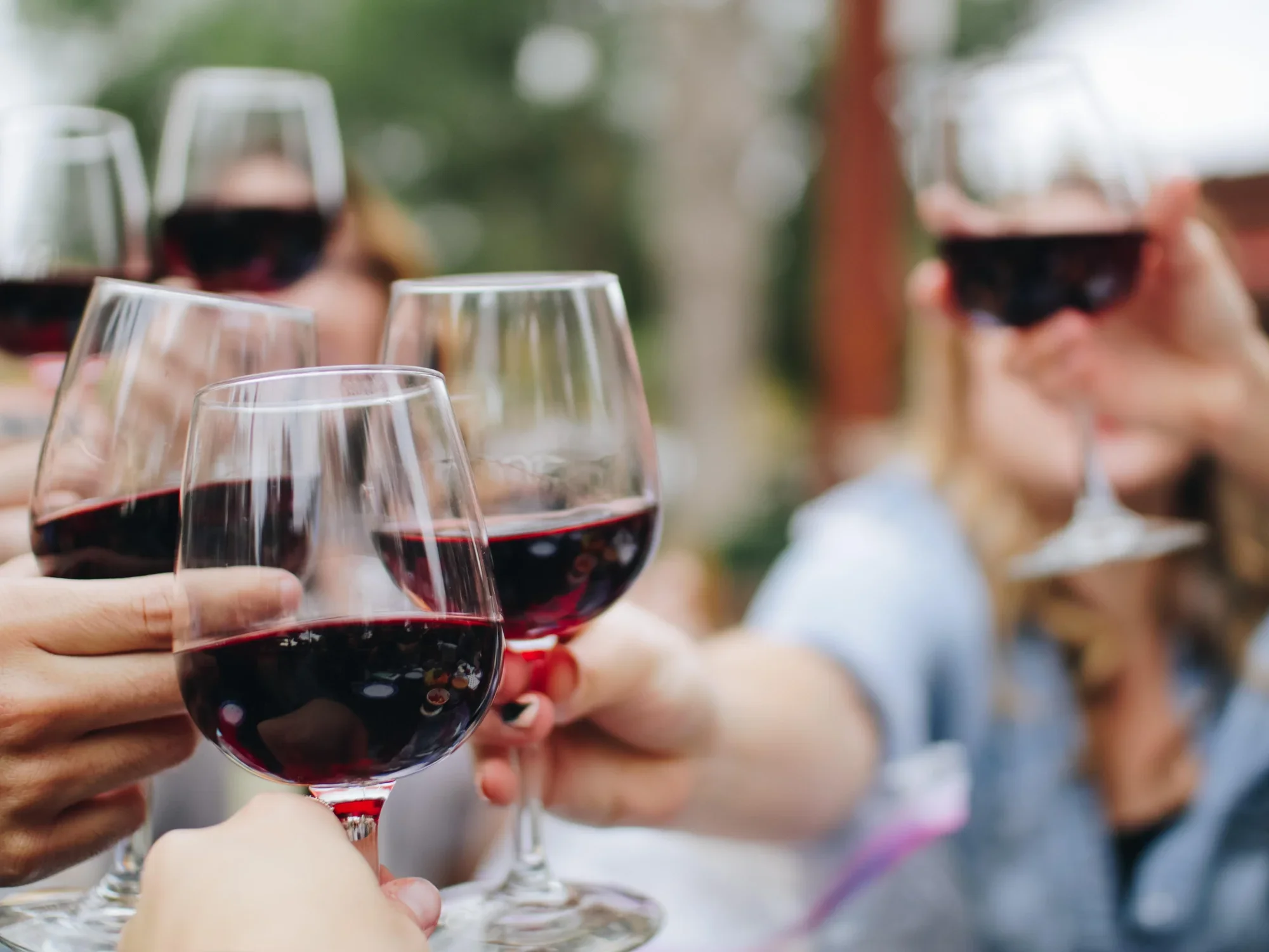 People clinking glasses of red wine outdoors during a social gathering.