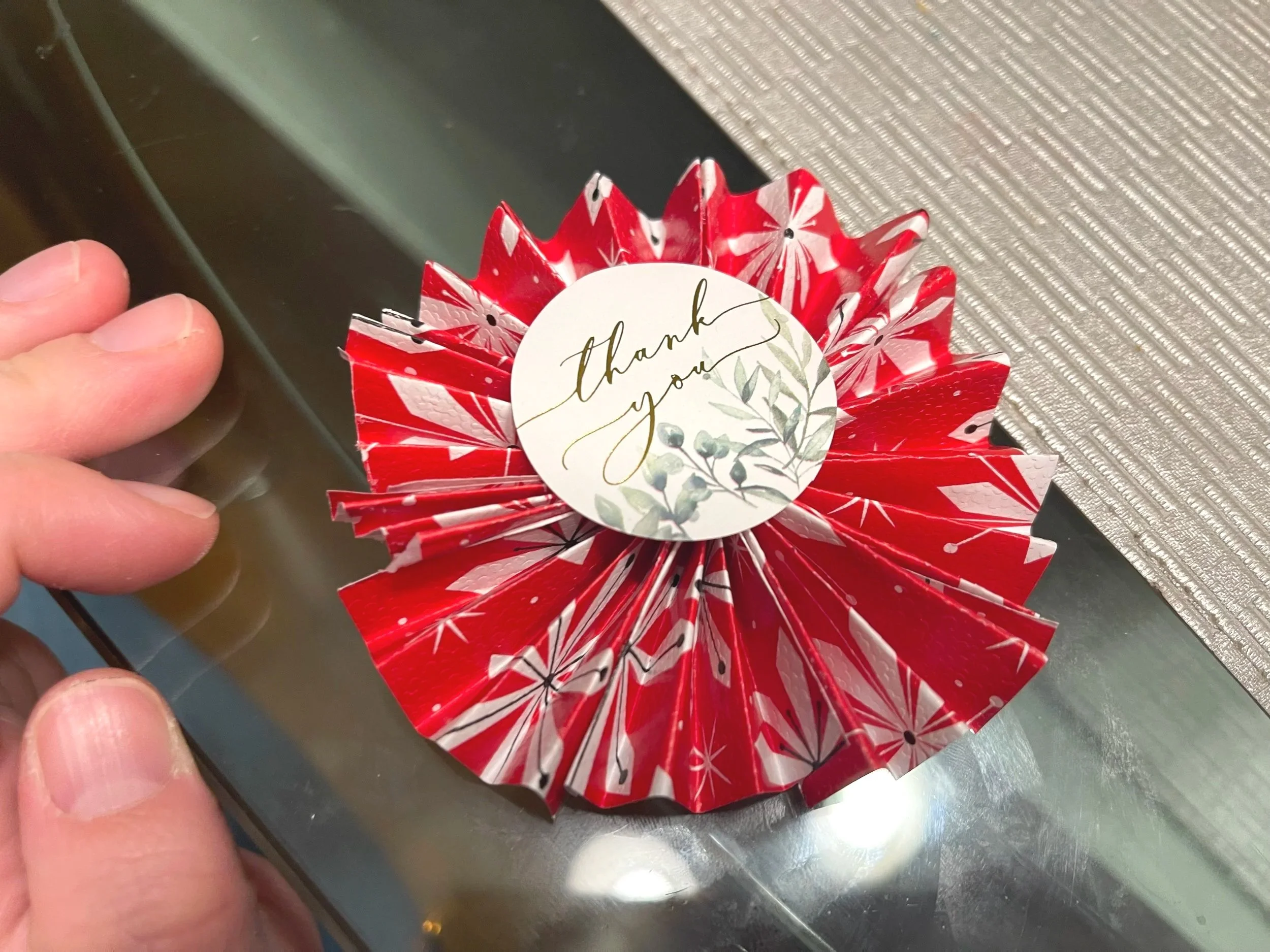 Red paper decoration with a circular white sticker that says 'thank you' and has green leaves illustration.