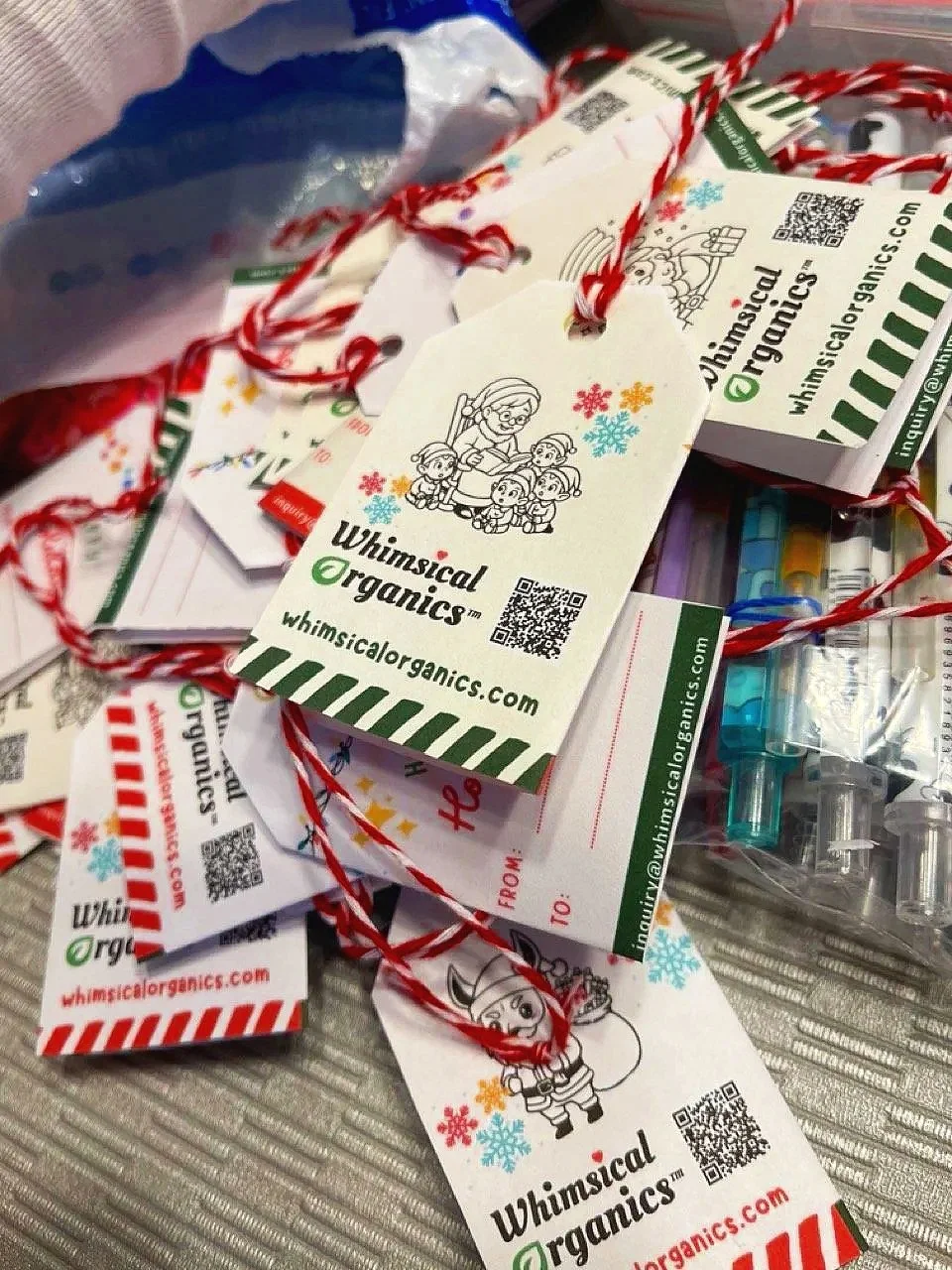 Assorted Christmas gift tags from Whimsical Organics with holiday illustrations and red and white striped string.