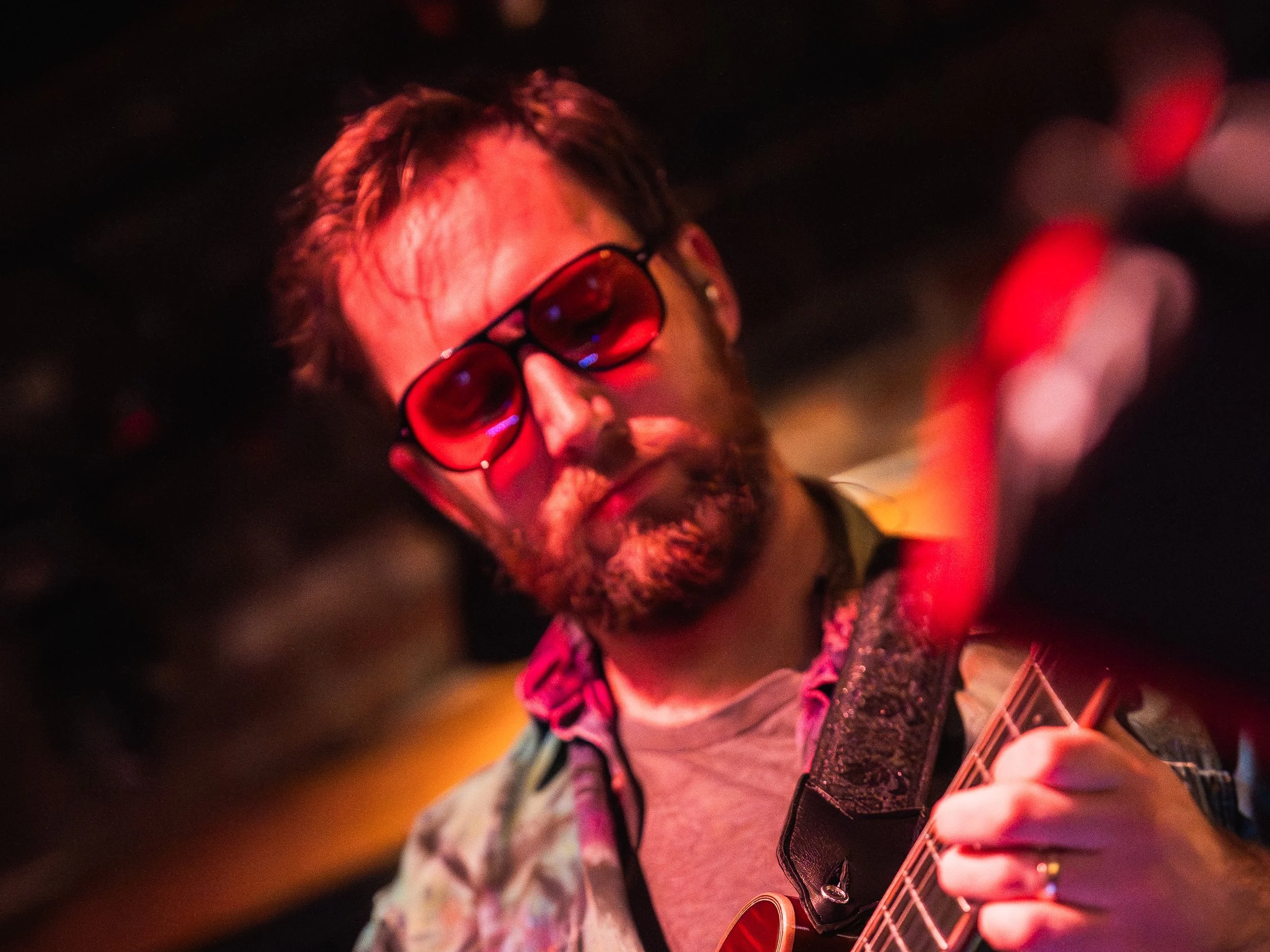 Dan Hiss playing lead guitar under red stage lighting.