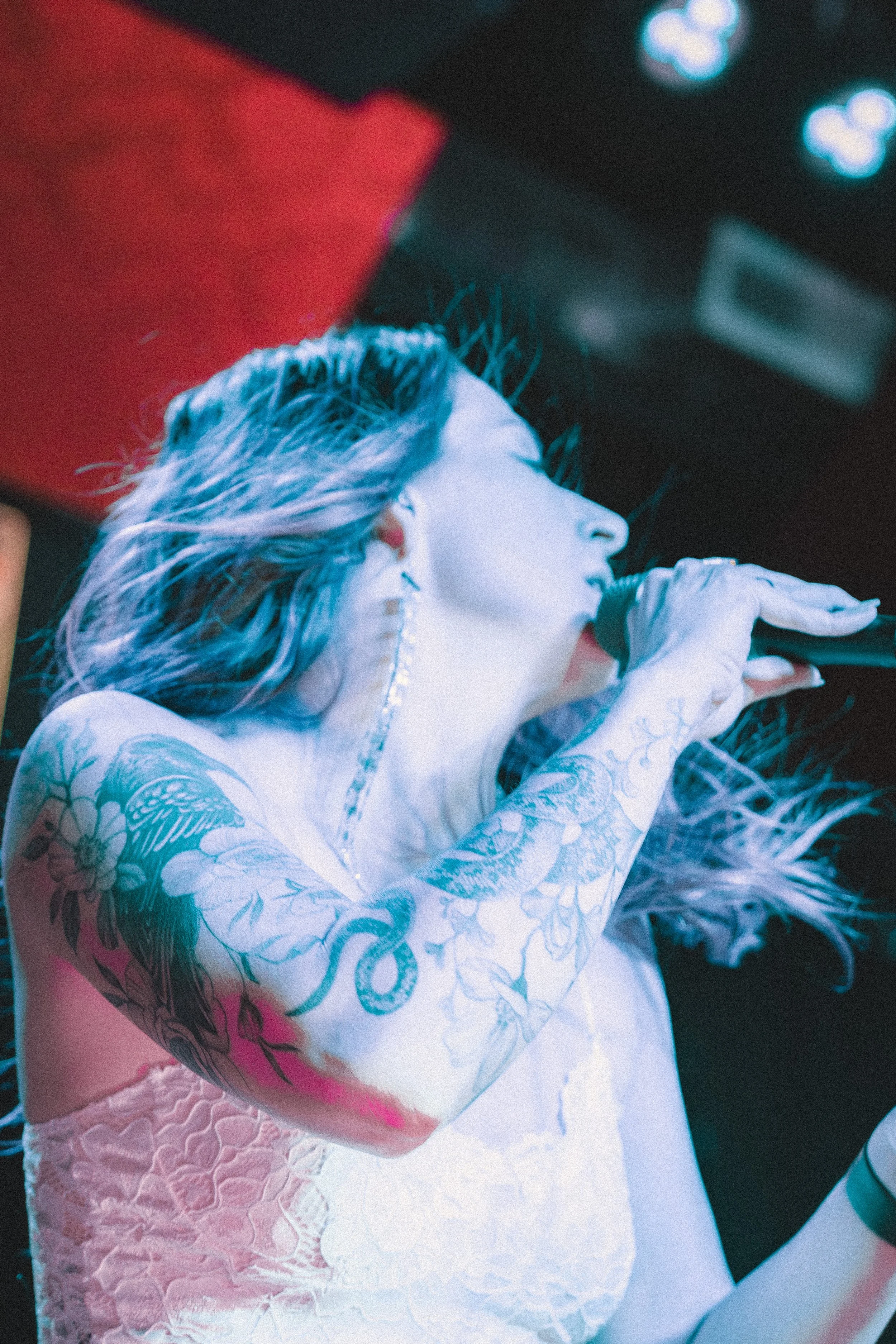 Liz Bauer singing into a handheld microphone under blue lighting.