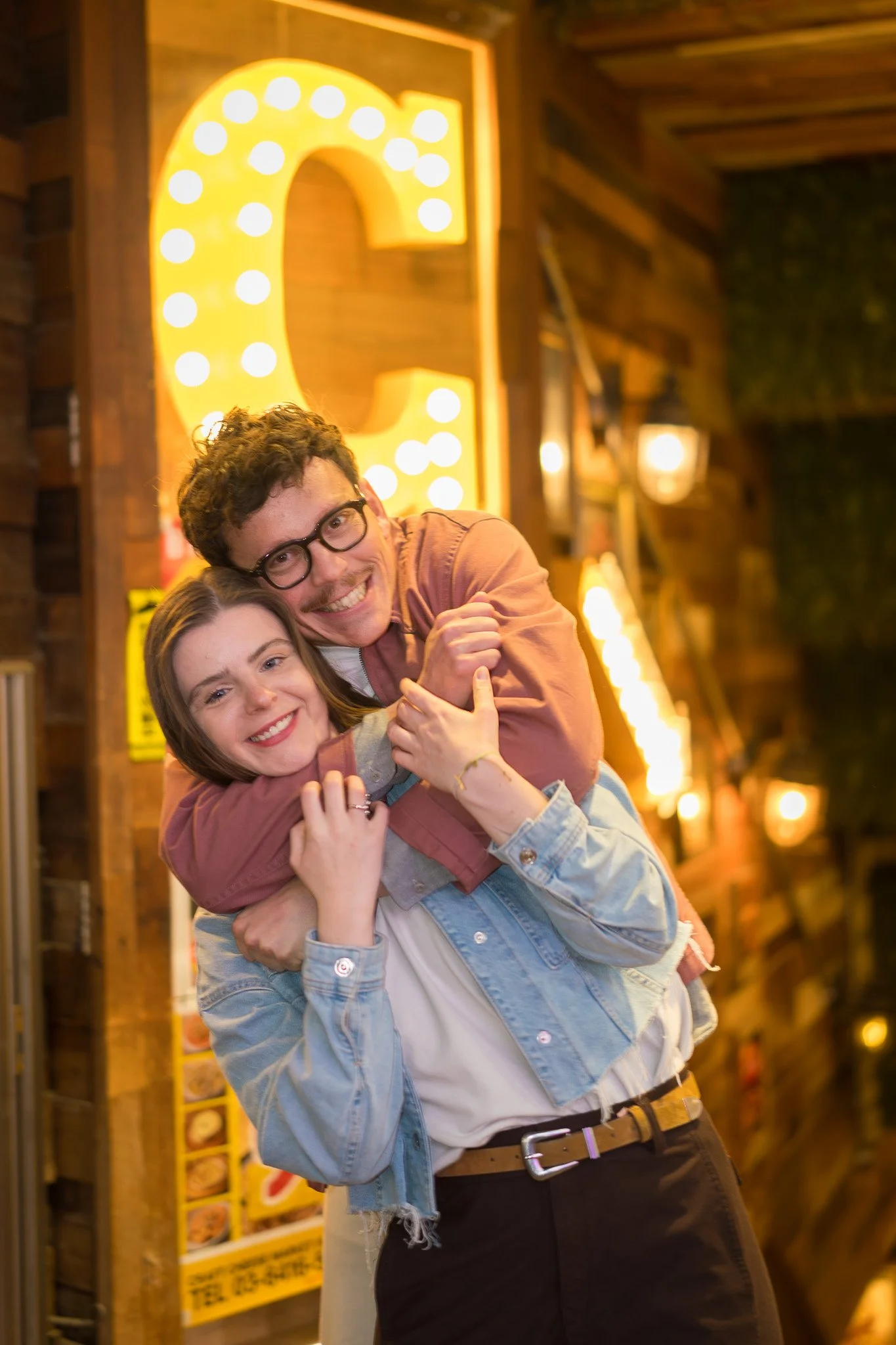 A happy couple hugging at night in front of a large illuminated letter C.