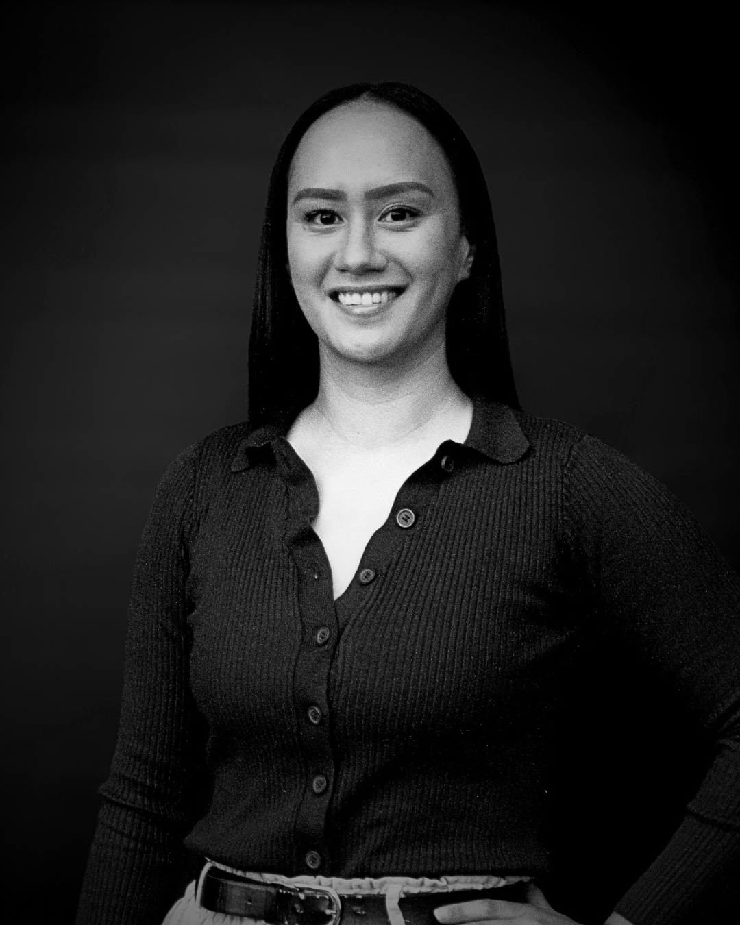 Portrait of a young woman with long dark hair, smiling, wearing a button-up shirt, against a dark background.