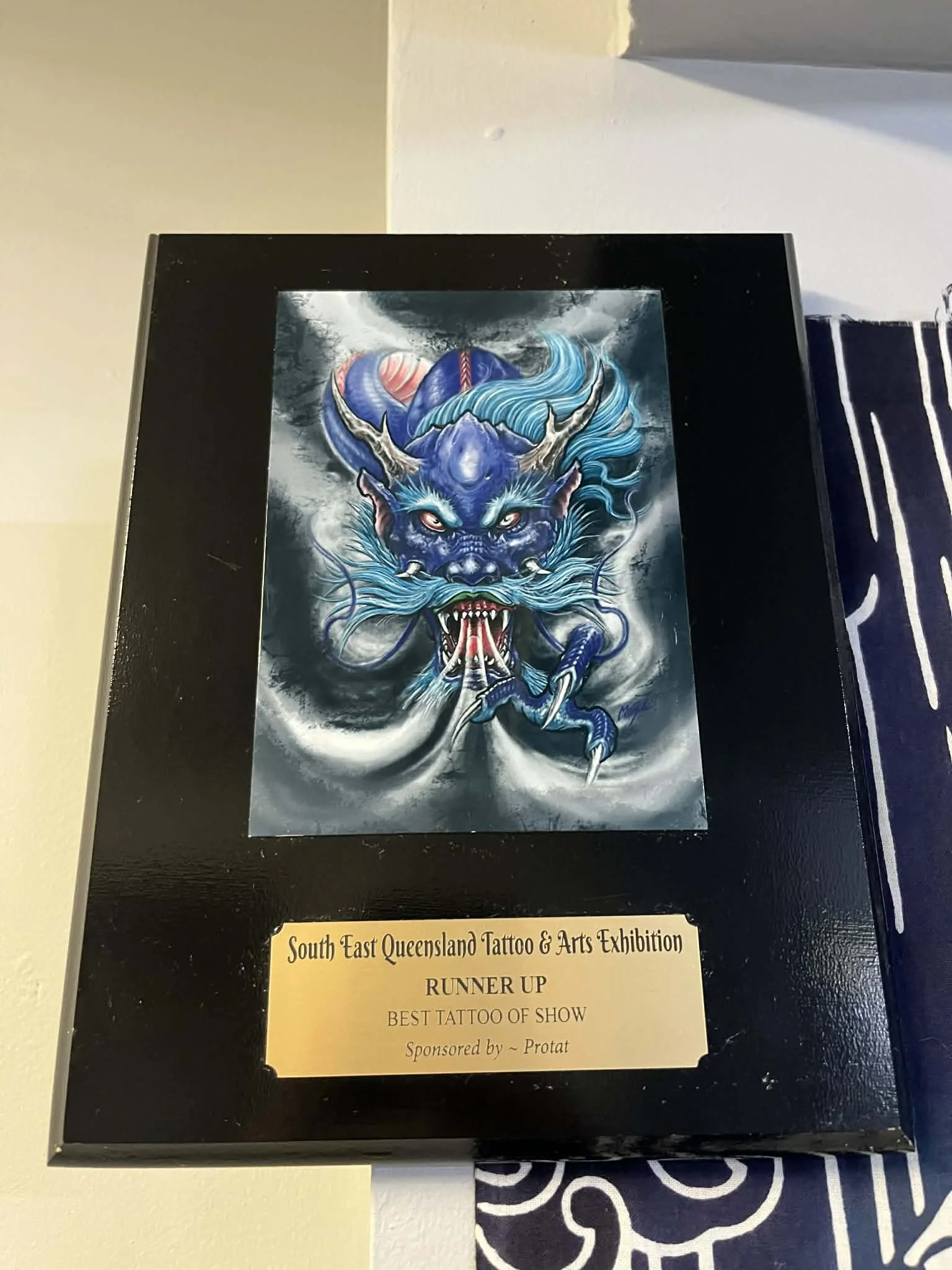 Tattoo award plaque for a dragon tattoo, titled 'South East Queensland Tattoo & Arts Exhibition'. The plaque indicates it was the runner-up for best tattoo of the show, sponsored by Protat.