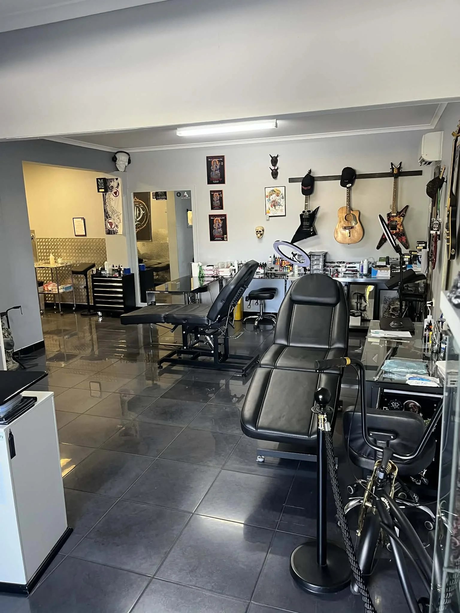 Tattoo studio with tattoo chairs, equipment, guitars, framed artwork, and tattoo supplies.