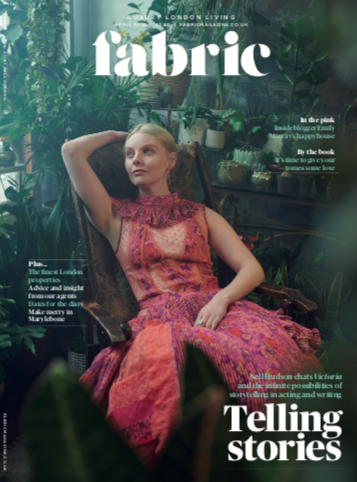 A woman in a pink and orange patterned dress sitting in a lush green greenhouse surrounded by plants.