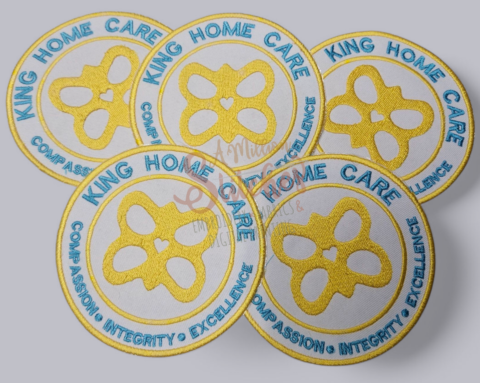 Five embroidered patches with a gold butterfly design, blue text reading 'King Home Care,' and words 'Compassion, Integrity, Excellence, Dedication' around the border.