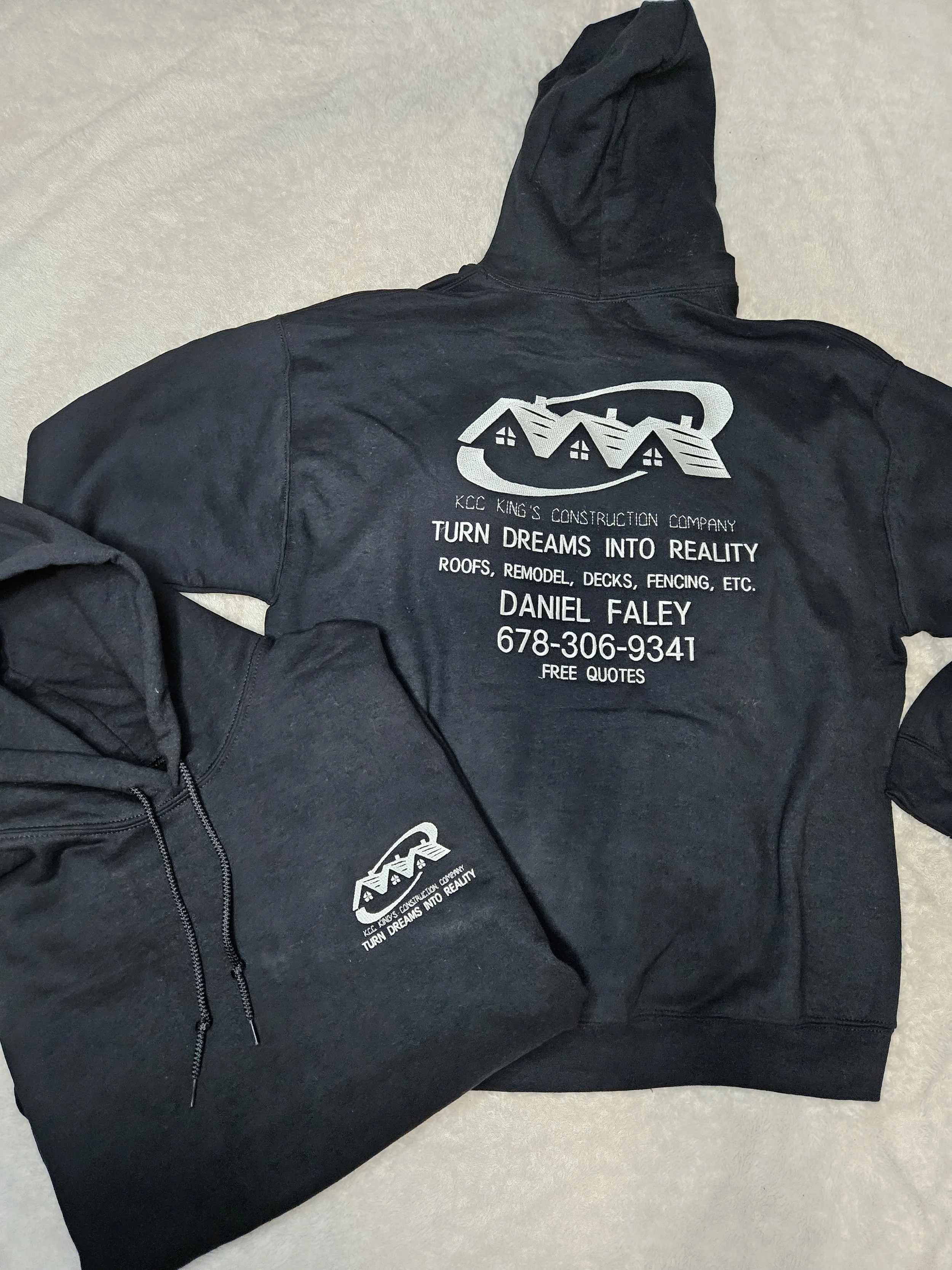 Black hoodie with a logo and contact information for KCC King's Construction Company, featuring a house graphic and slogan 'Turn dreams into reality'.