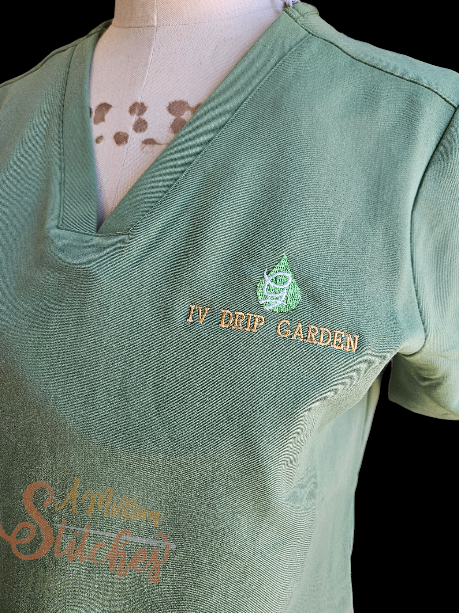 Close-up of a light green polo shirt on a mannequin with embroidery that reads 'IV DRIP GARDEN' and a green leaf logo.