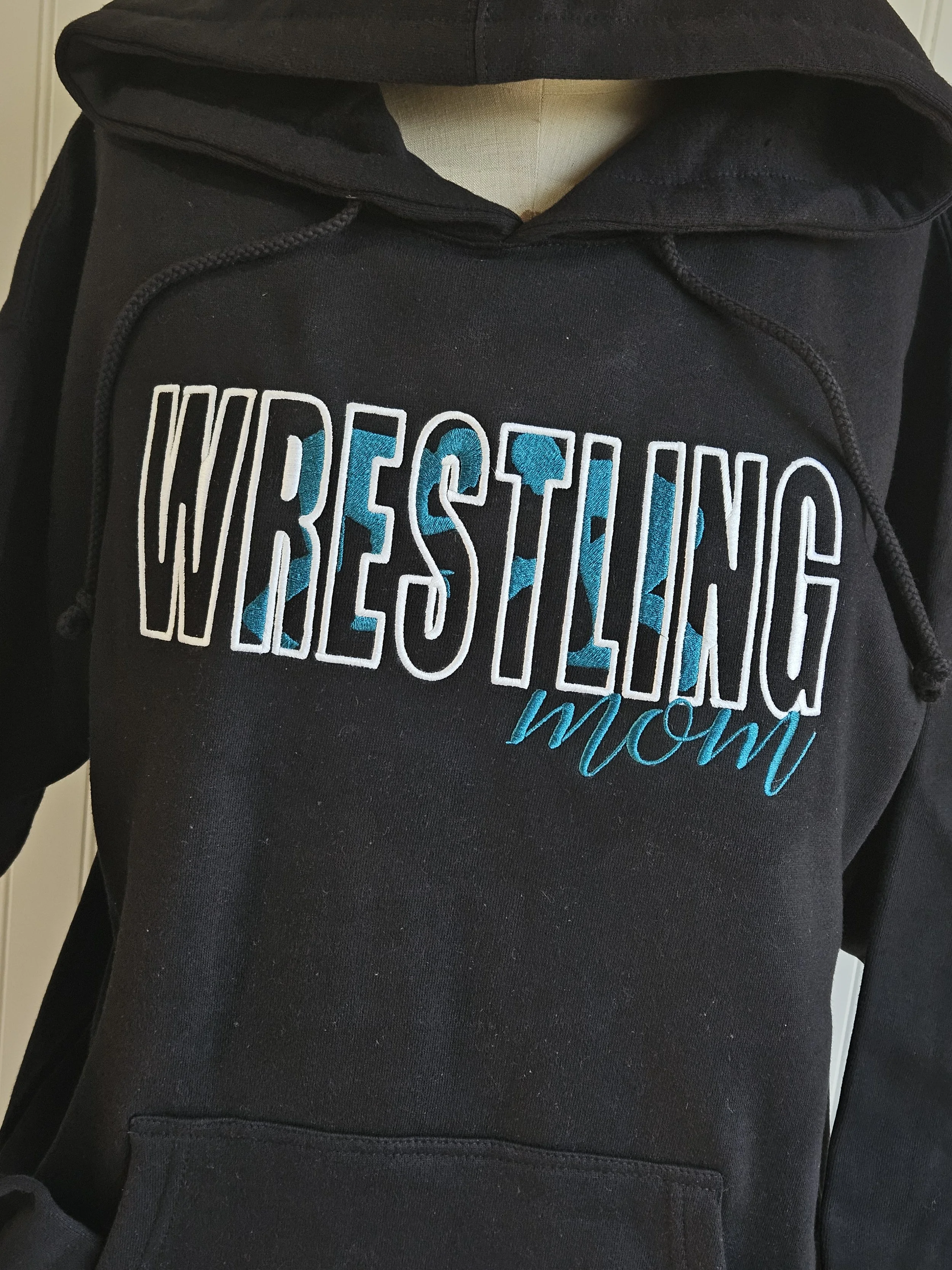 Black hoodie with embroidered text that says 'Wrestling Mom' in white and blue.