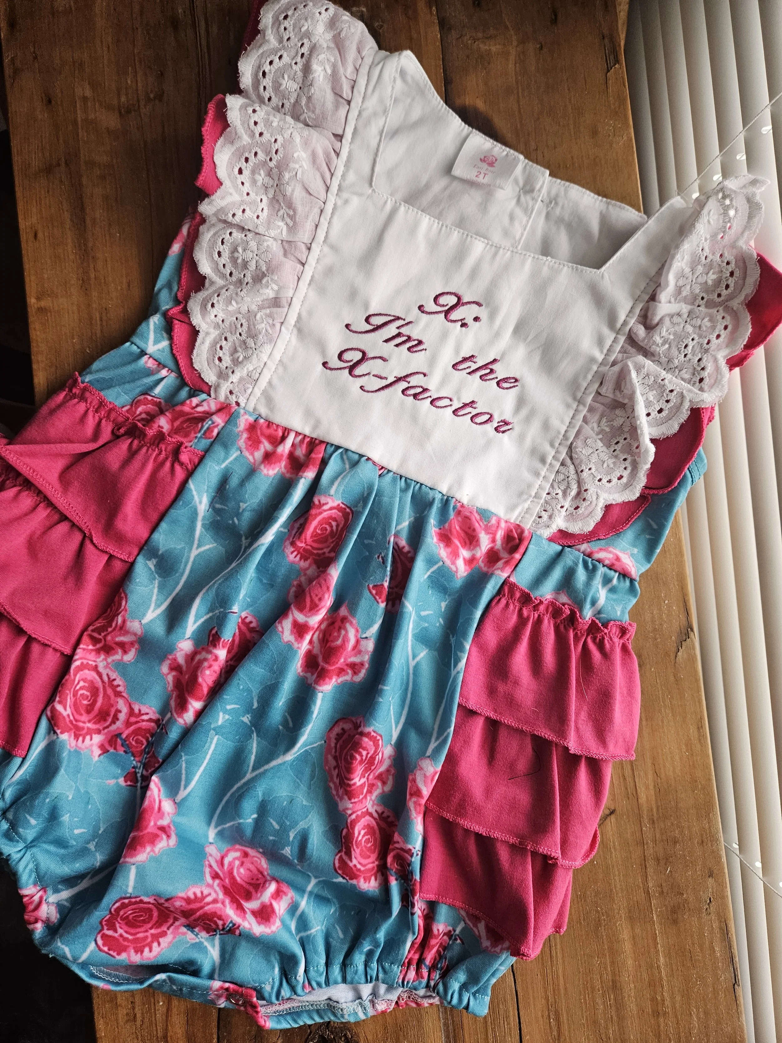 Child's dress with a white embroidered top saying 'Hi. I'm the Teacher' and a pink and blue floral skirt with ruffled pink layers.