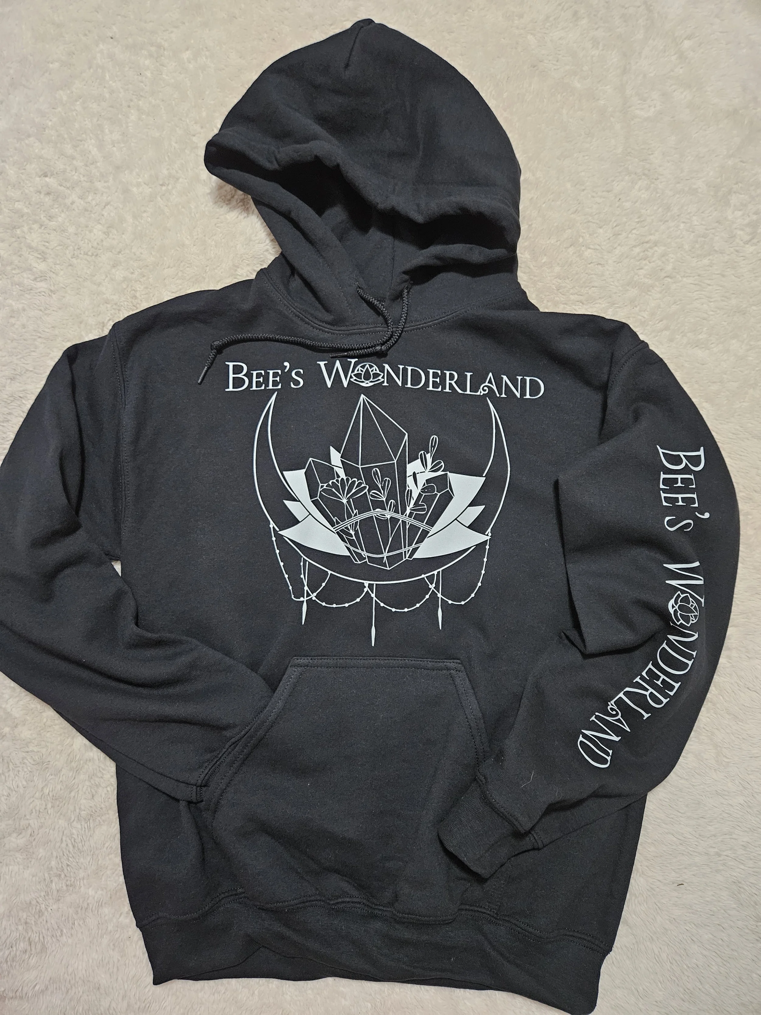 Black hoodie with white graphic design and text reading "Bee's Wonderland" on the front and sleeve, featuring a crystal or geometric shape with bee and plant motifs.