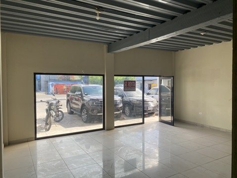 Empty commercial space with large glass windows and a view of parked cars and motorcycles outside.