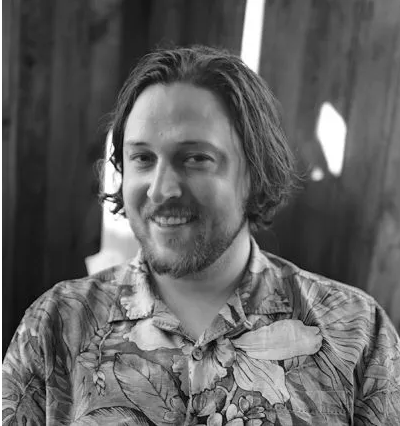 Black and white photo of a man with long hair and beard, resting his head on his hand.