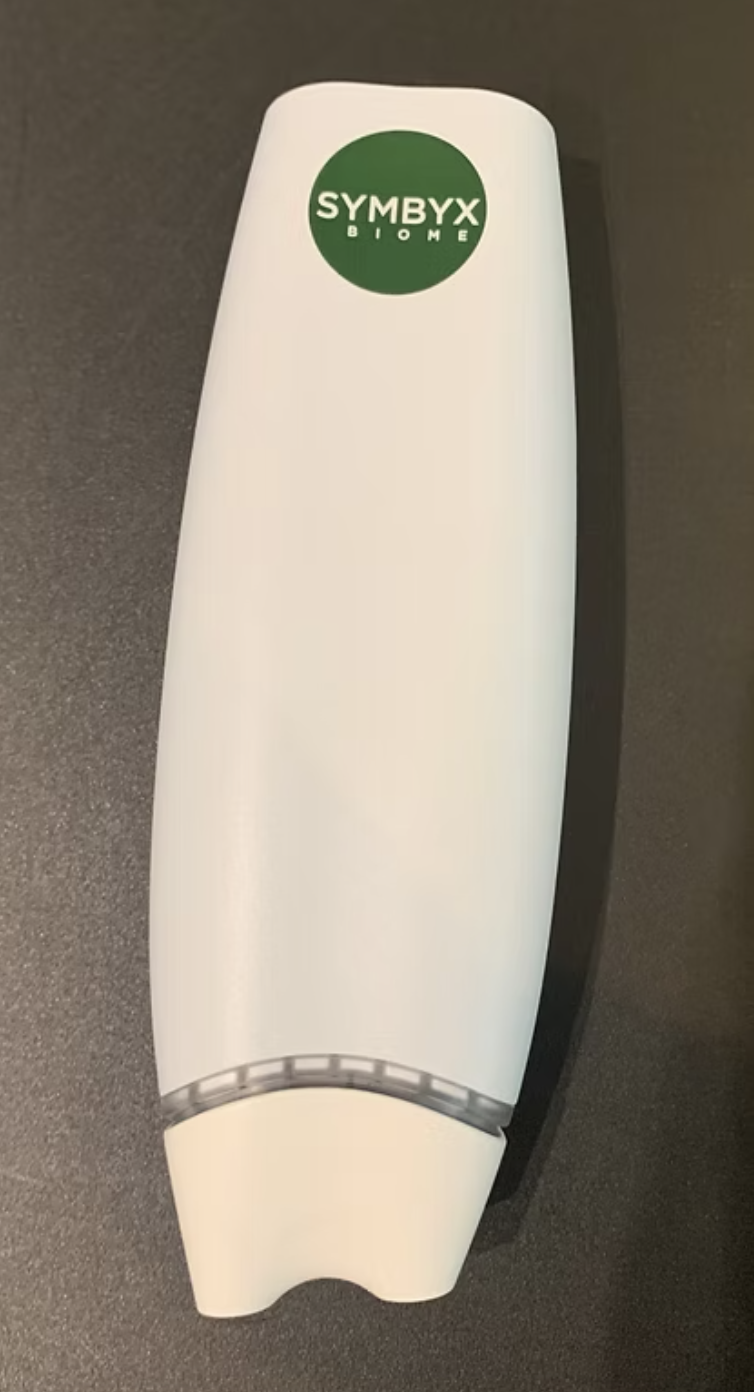 A white device with a green circle logo that reads "SYMBYX BIOME" on a dark surface.