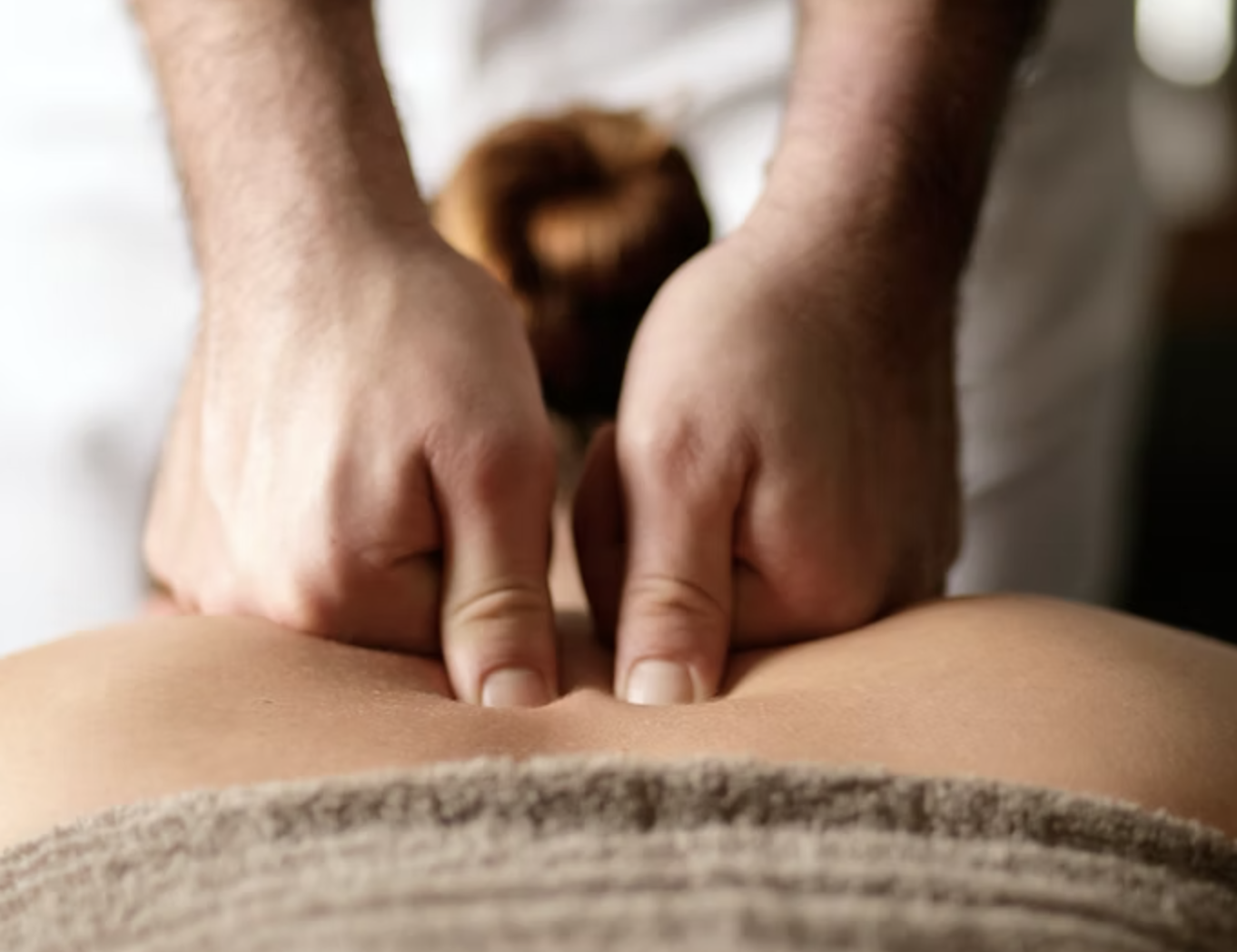 Close-up of a person receiving a massage on their lower back with the therapist's hands pressing on the skin.