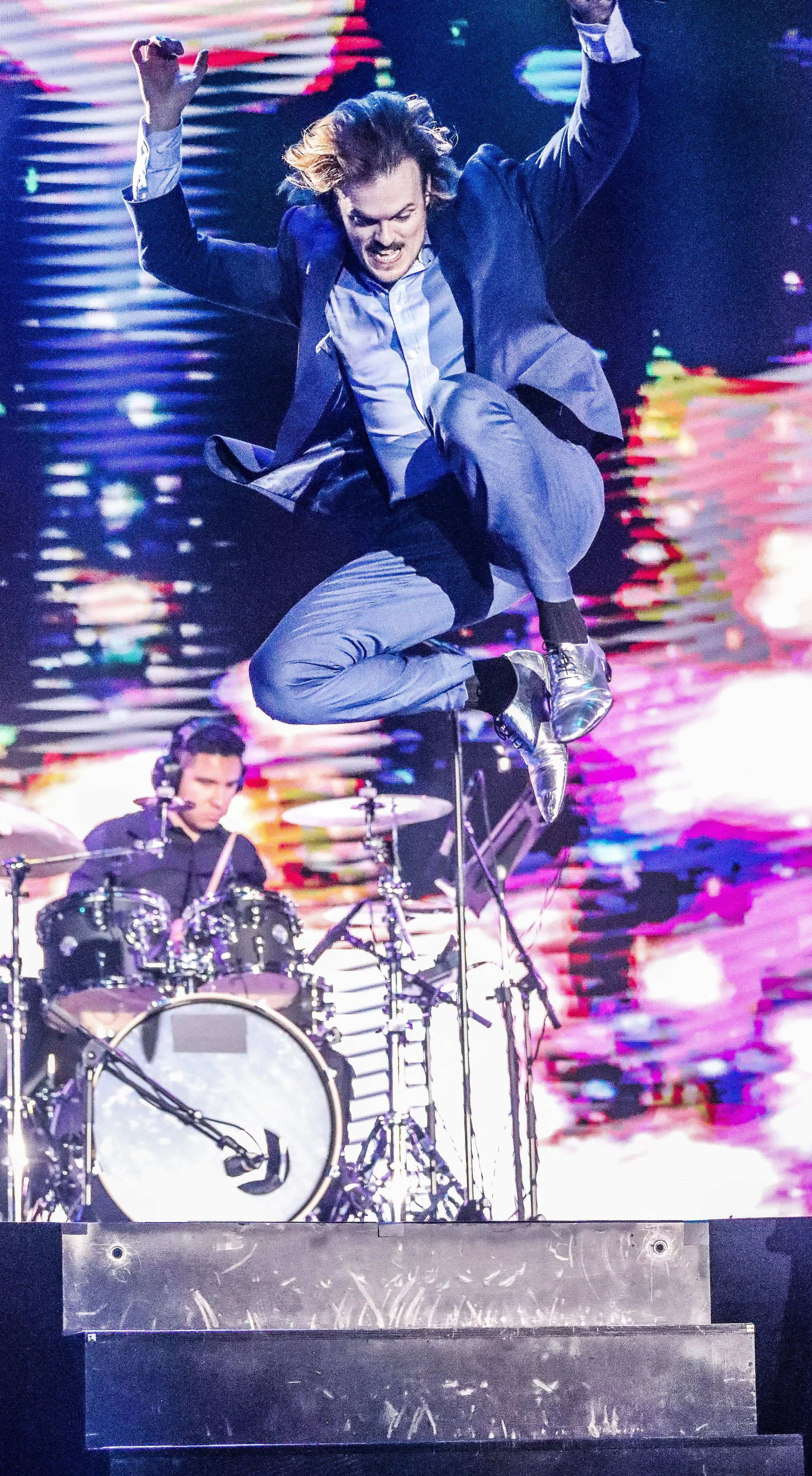 Max Adam, dressed in blue suit, in mid-jump from the stage during one of his rock concert performances