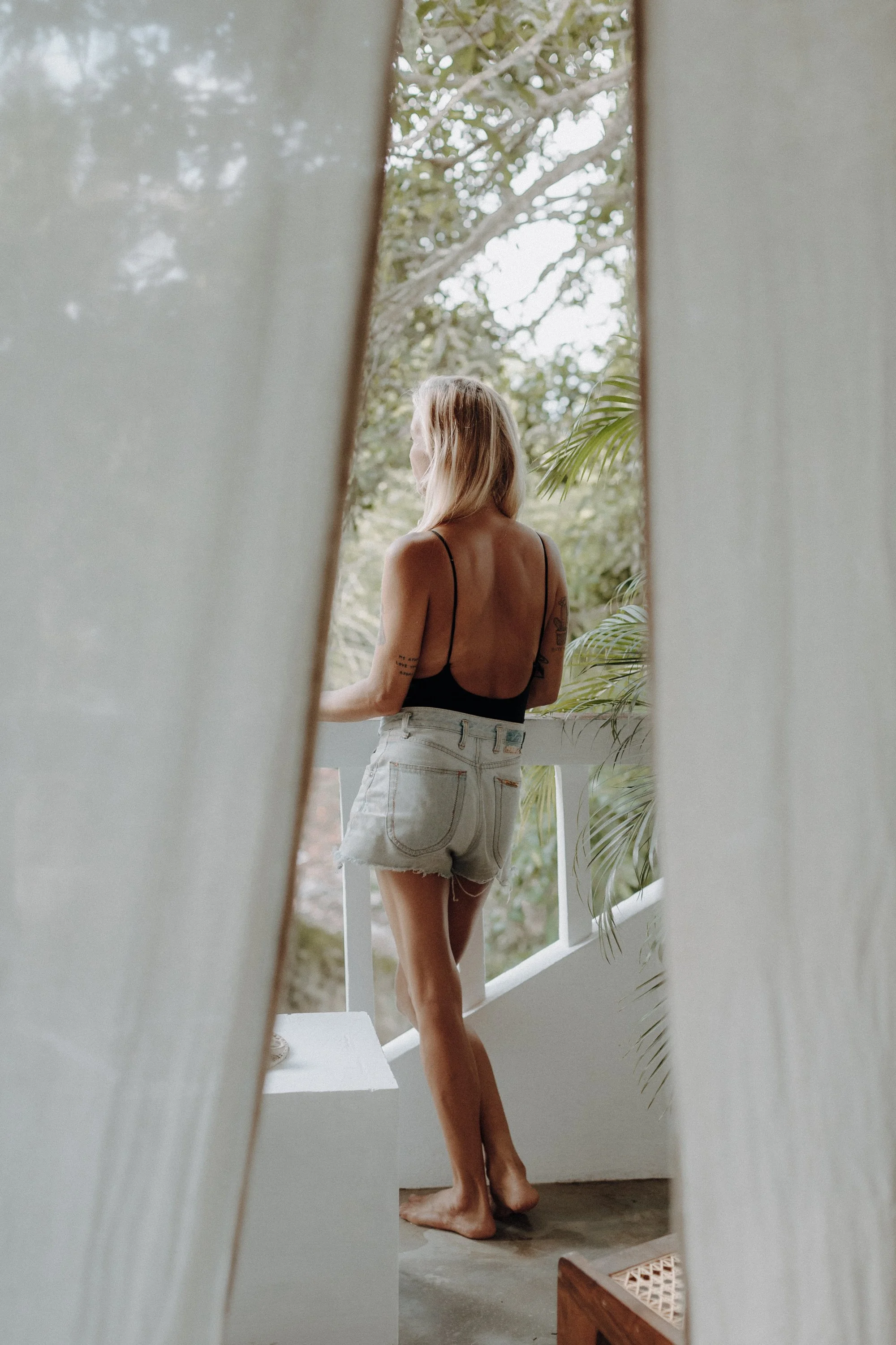 Guest standing barefoot on the Earthlinks balcony, seen through a partially open curtain with greenery in the background.