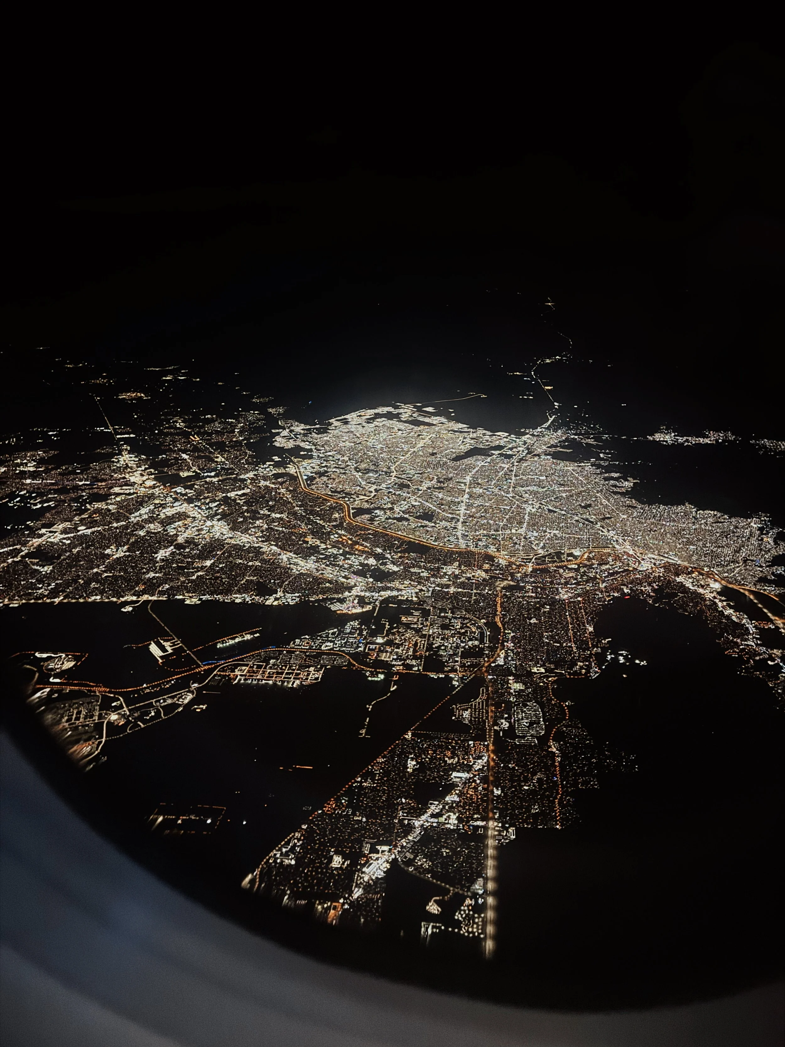 Aerial night view of a city with illuminated streets and buildings, seen from an airplane window.