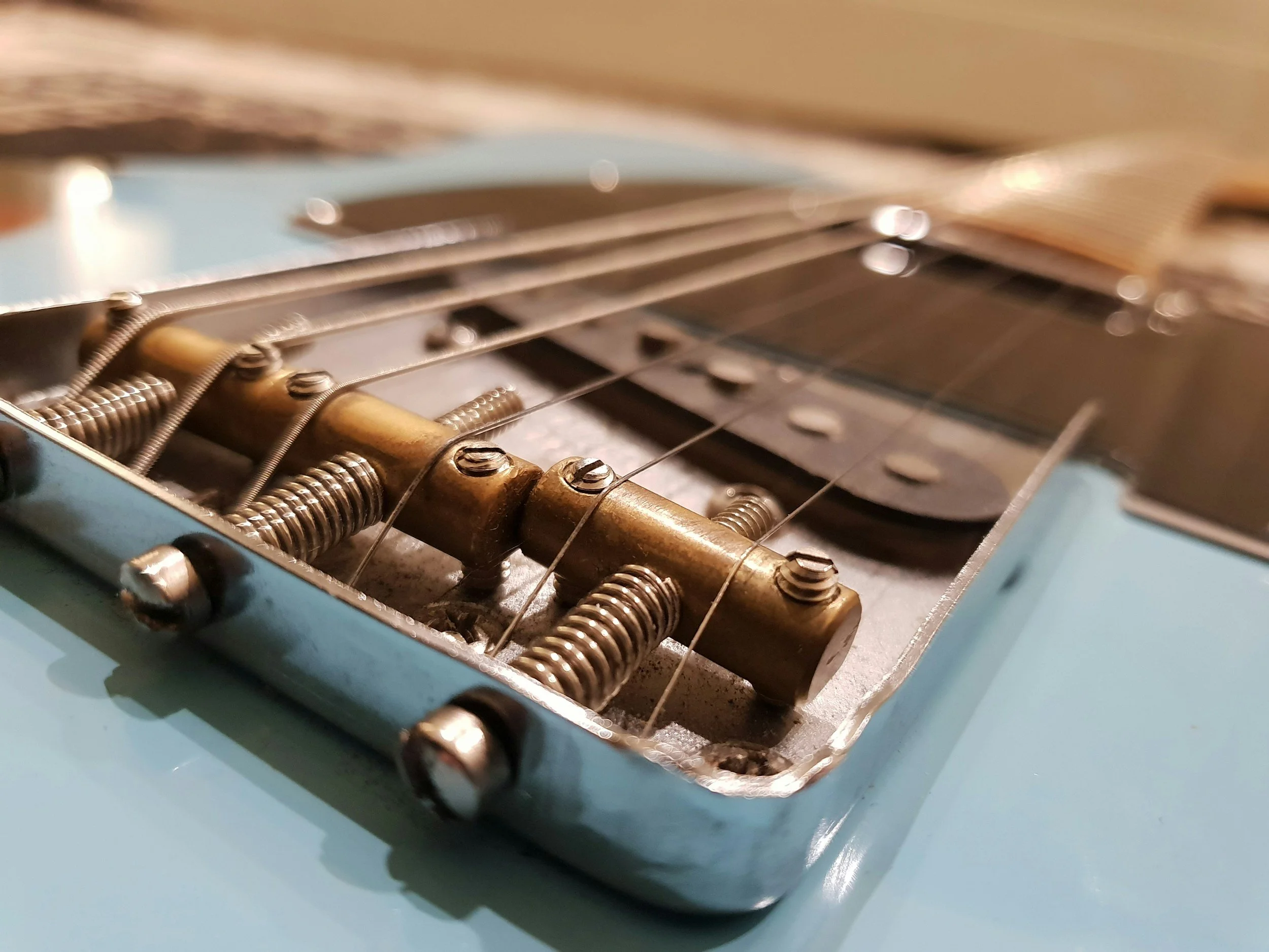 Close-up of a guitar bridge with strings, metal saddles, and springs, on a light blue guitar body.