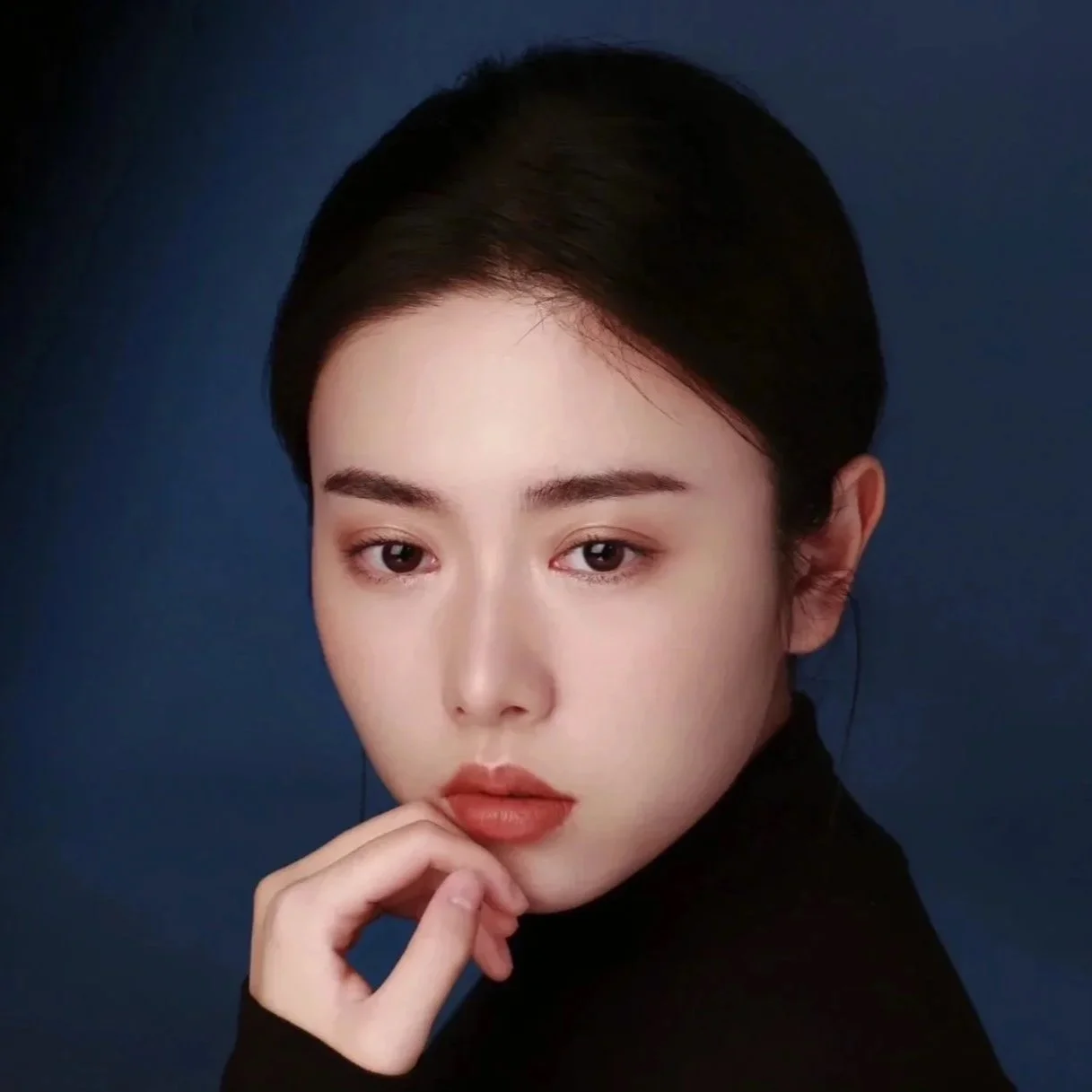 Portrait of a young woman with dark hair and light skin, wearing a black top, against a dark blue background.