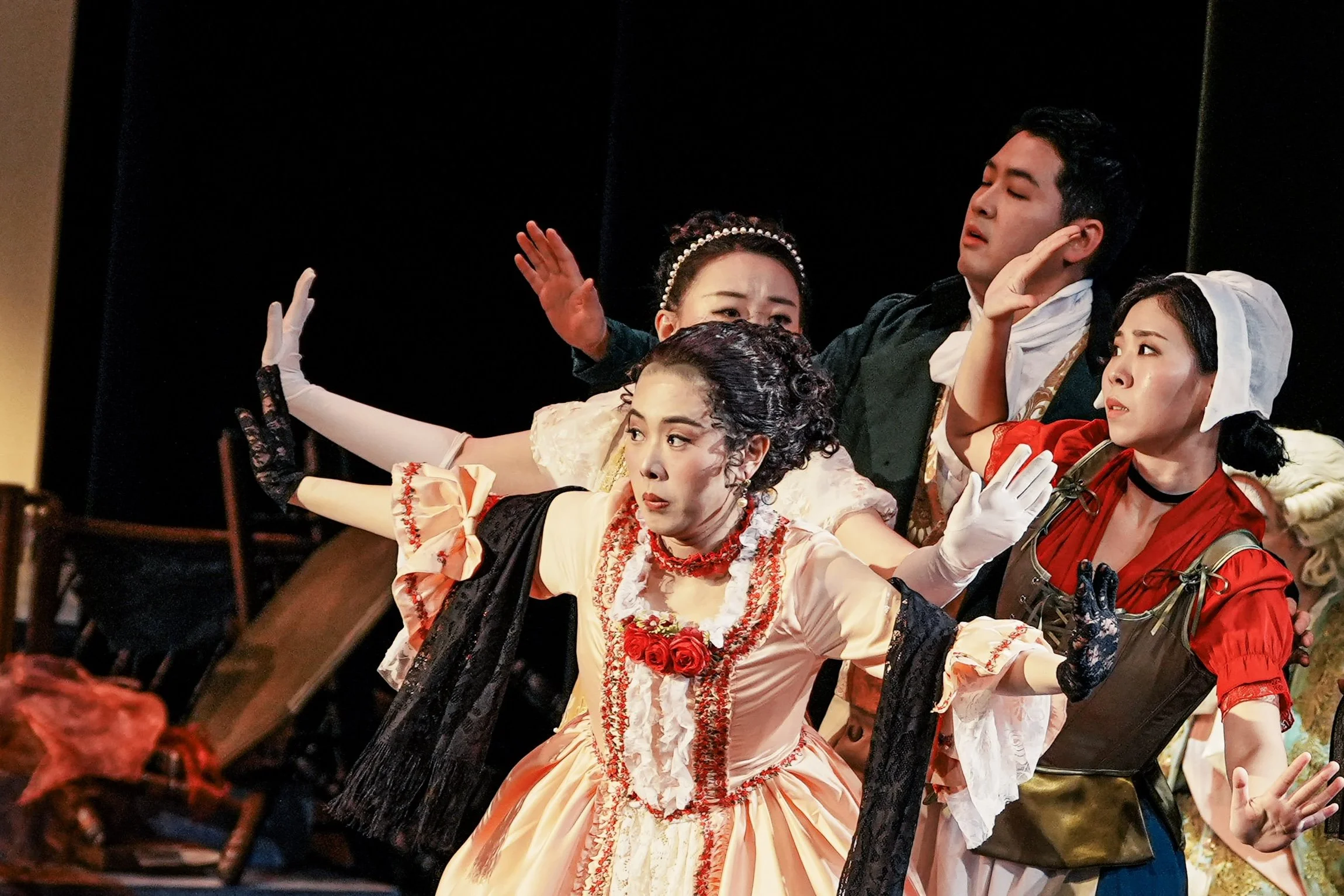 Theater scene with actors in period costumes performing on stage, displaying expressive gestures and facial expressions.