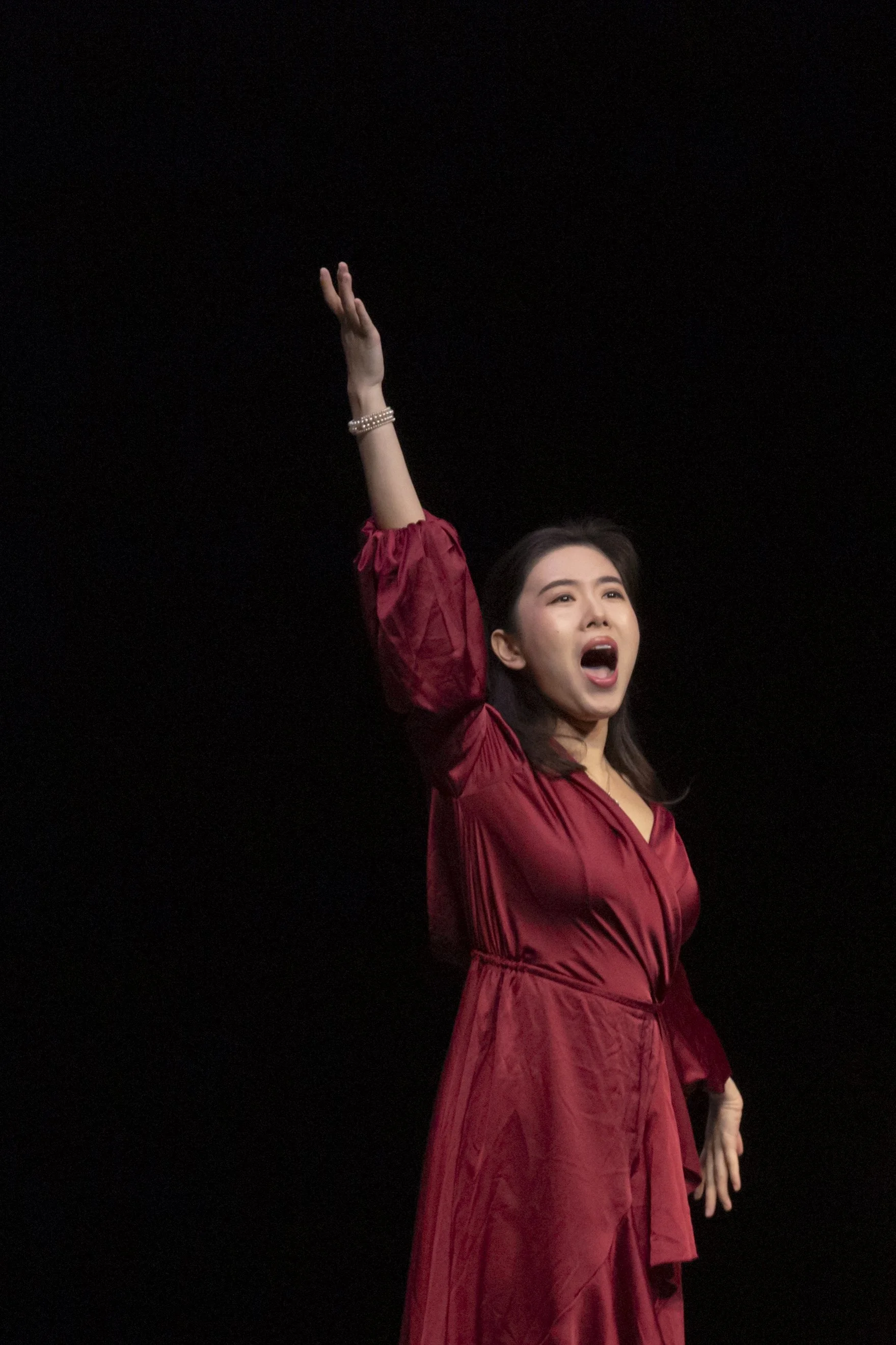 Young woman in red dress performing on stage with arm raised and mouth open.