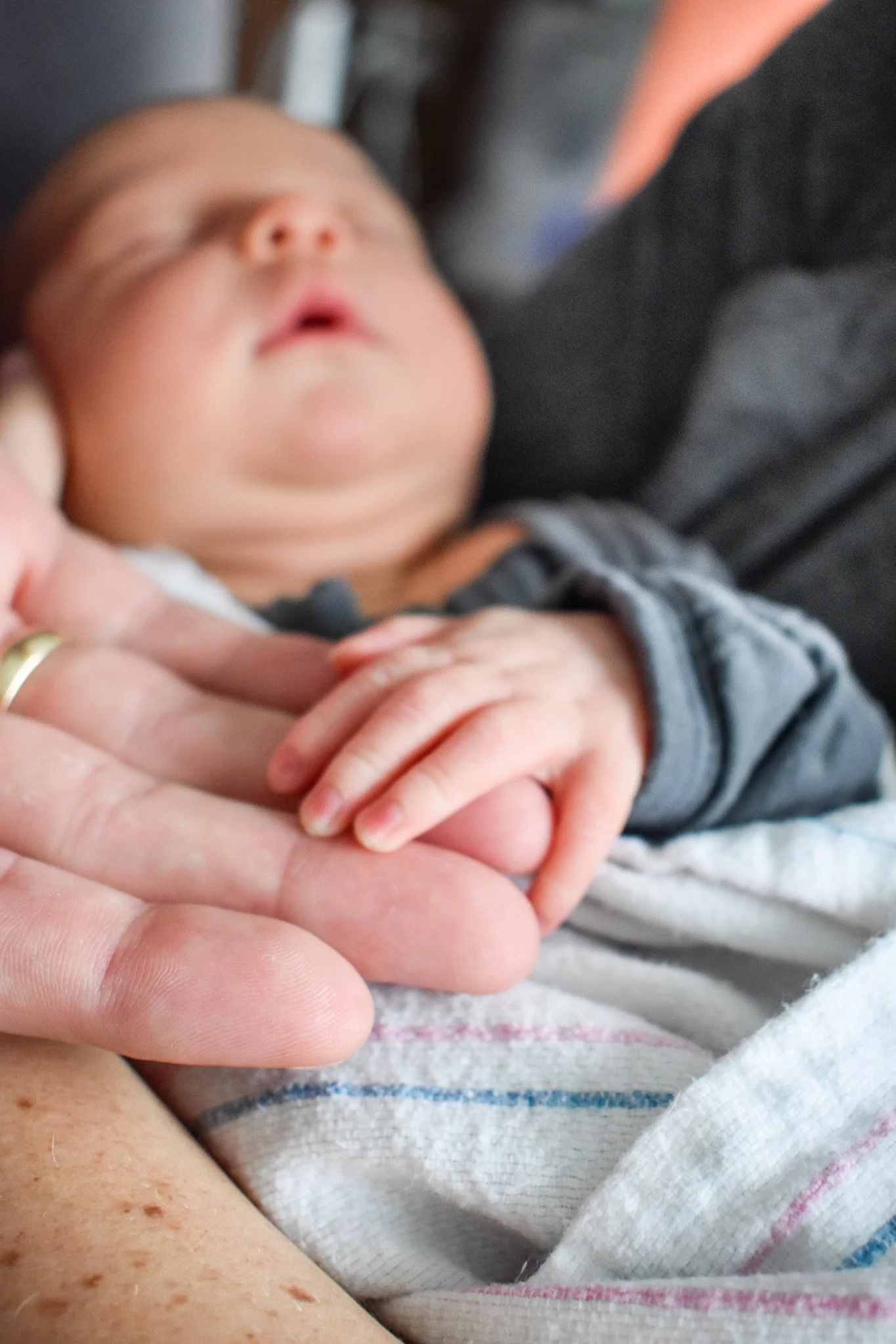 Close-up of a newborn baby sleeping and holding an adult's finger.