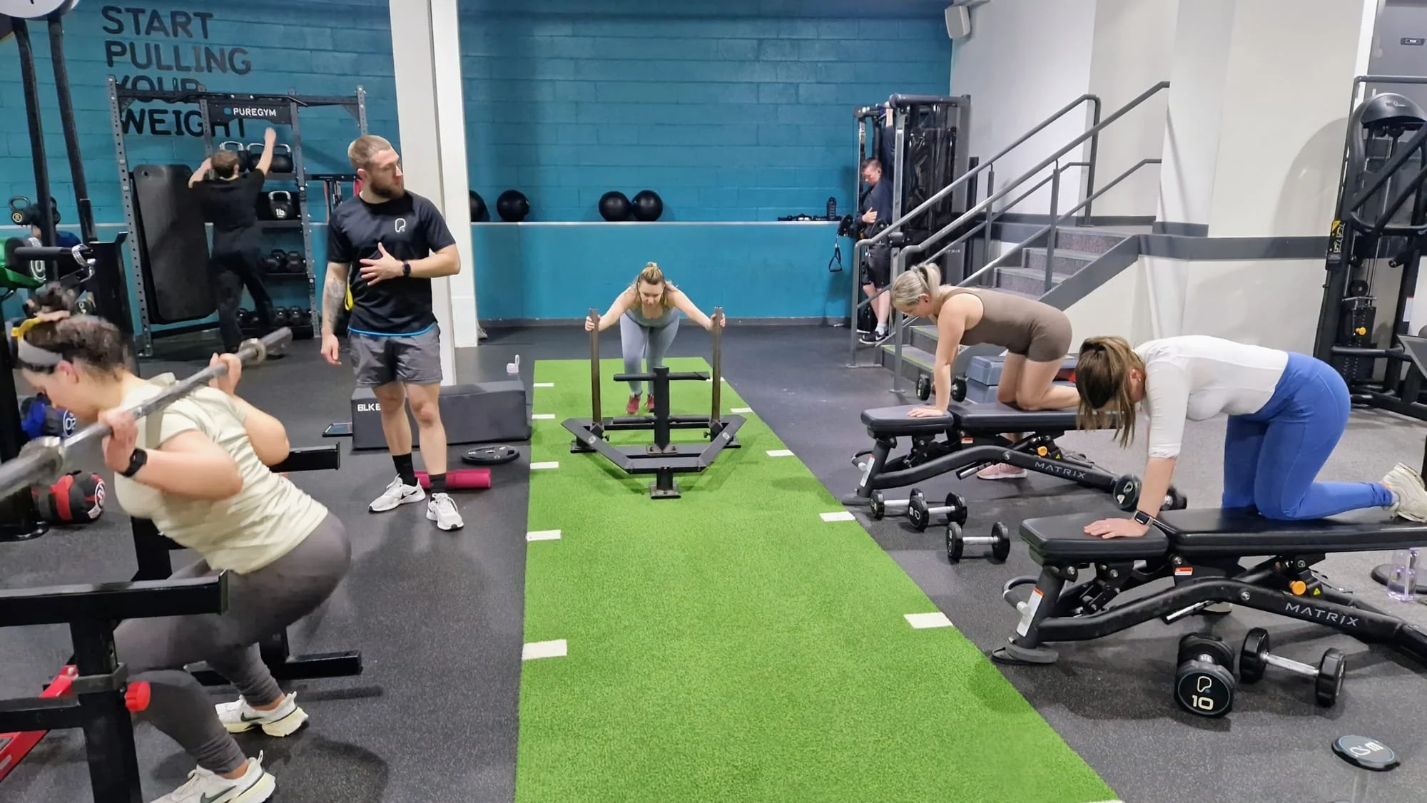 People exercising in a gym, doing various workout activities including squats, lifting weights, and using treadmill.