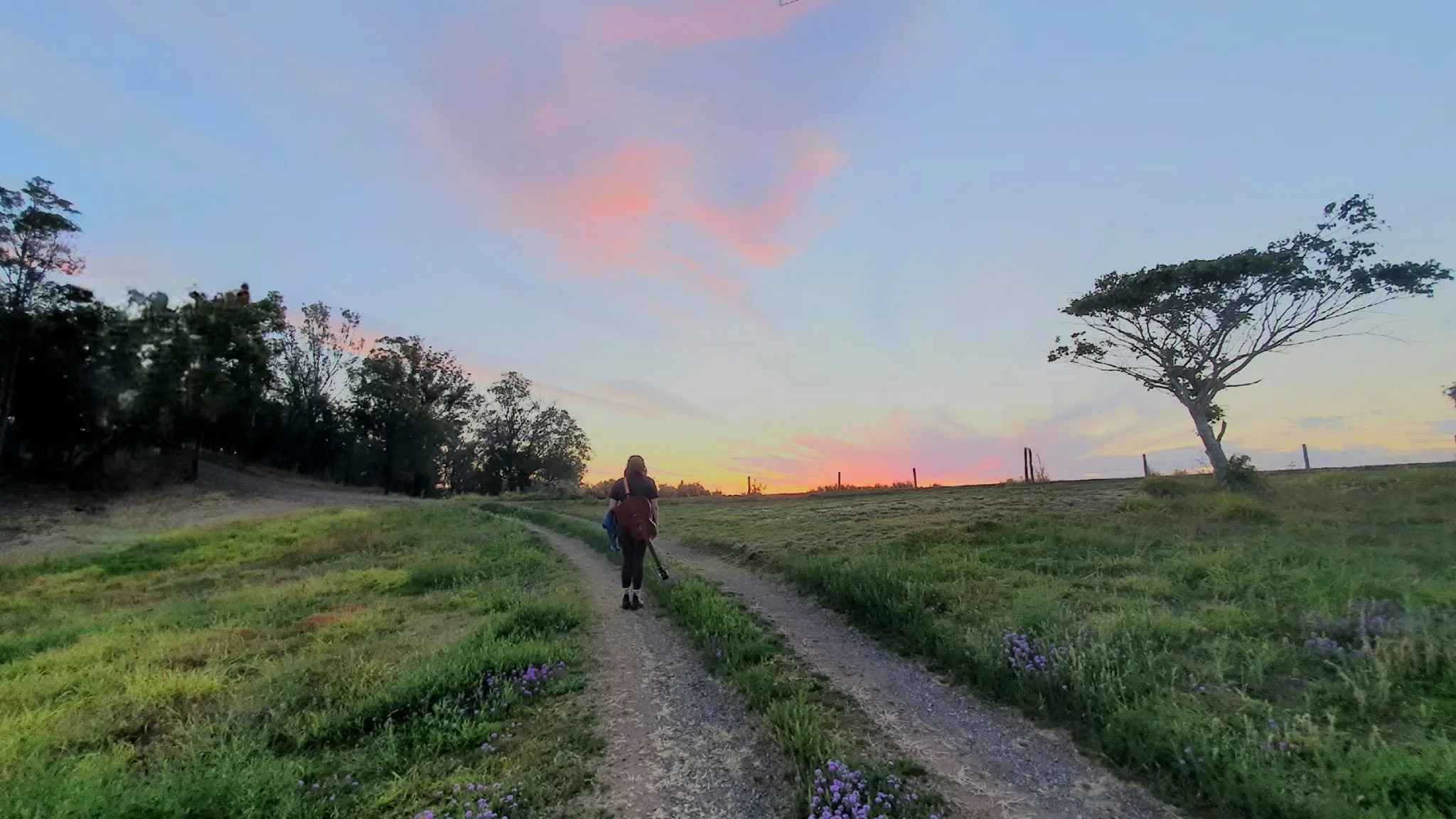 Tahnee Georgia walking on a dirt path at sunset, with trees on either side and a pink and blue sky.