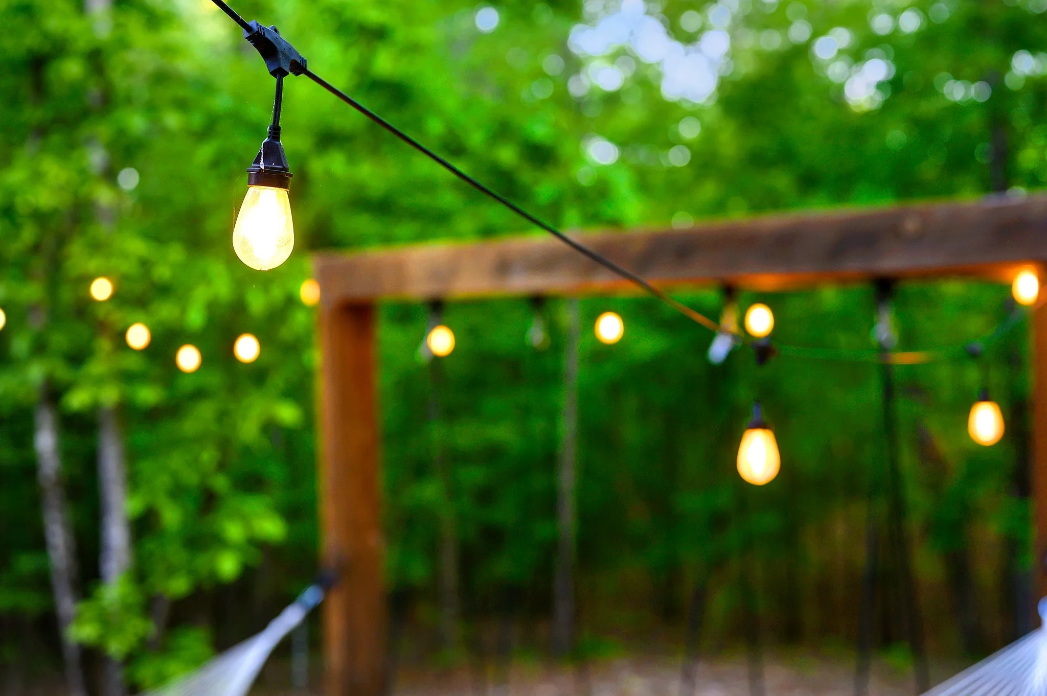 String of outdoor string lights hanging in a wooded area with a hammock.