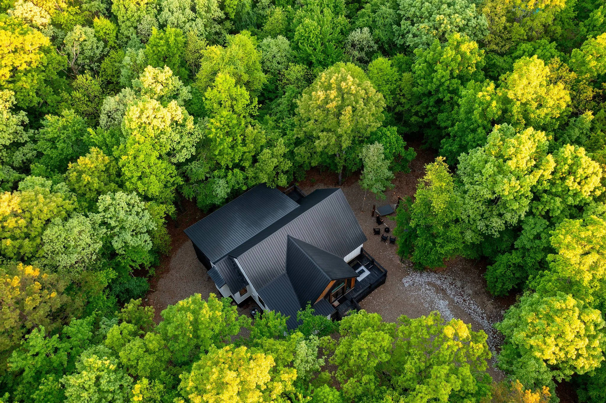 An aerial view of Hygge Hill, a modern cabin, surrounded by dense green trees with outdoor seating area.