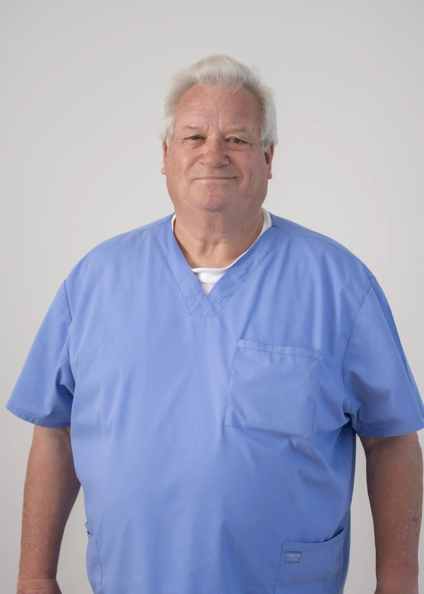 Portrait of Geoff Martin, Extended Care Paramedic, wearing light blue clinical scrubs and smiling warmly.