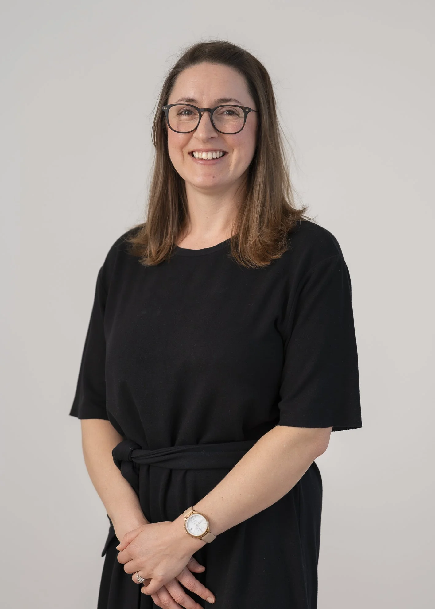 Portrait of Sam Buchanan, Sonographer, smiling in a black top and glasses against a neutral background.