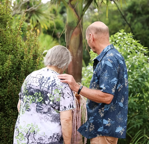 An elderly woman and a man looking at her garden, with the man touching the woman's shoulder.