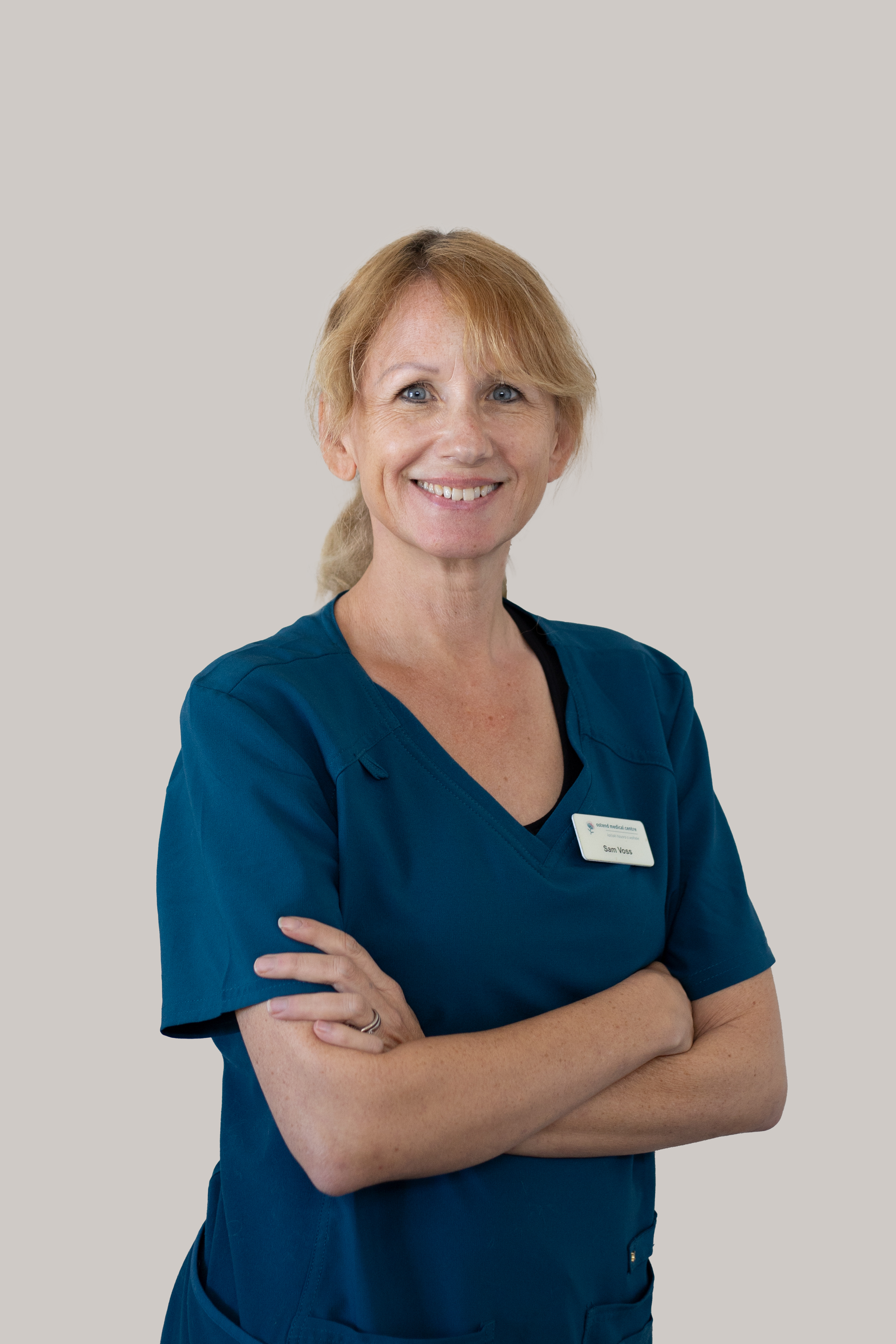 Portrait of Samantha Voss, Practice Nurse, smiling in teal scrubs with arms crossed.