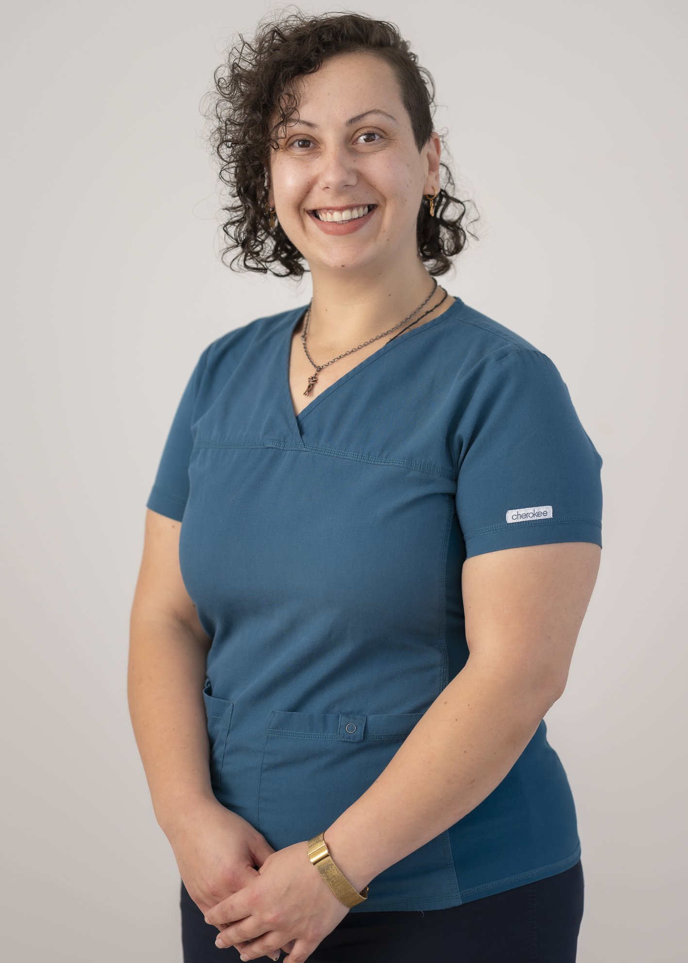 Portrait of a Practice Nurse, smiling in teal scrubs against a neutral background.