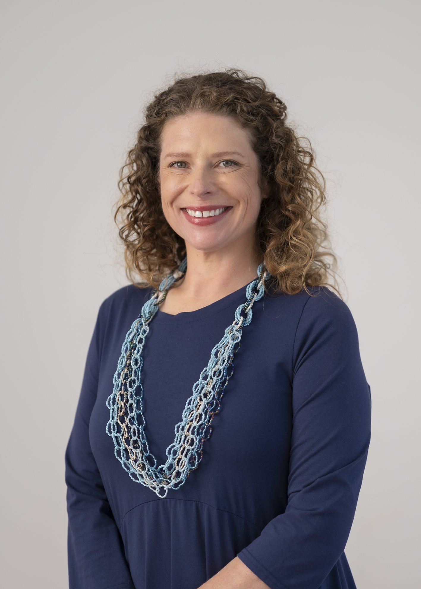Portrait of Gilian Graham, General Practitioner, smiling in a navy top with curly hair and a blue woven necklace.