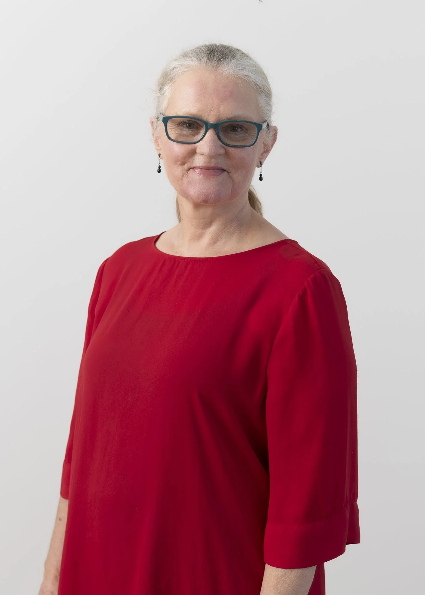 Portrait of Rozanne Gold, Social Worker and Health Improvement Practitioner, wearing a red top and blue glasses with a calm expression.