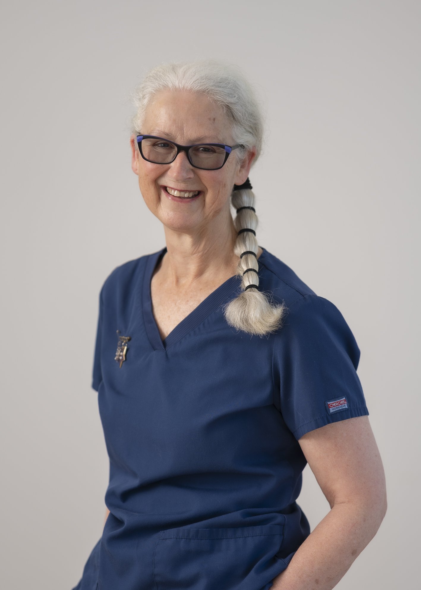 Portrait of Ellen Sumpter, Specialist Community Nurse, smiling in navy scrubs with glasses and braided white hair.