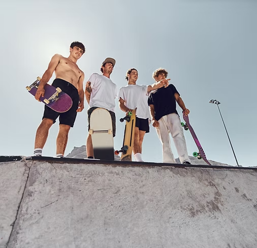 Four young men with skateboards standing on the edge of a skate ramp outdoors.