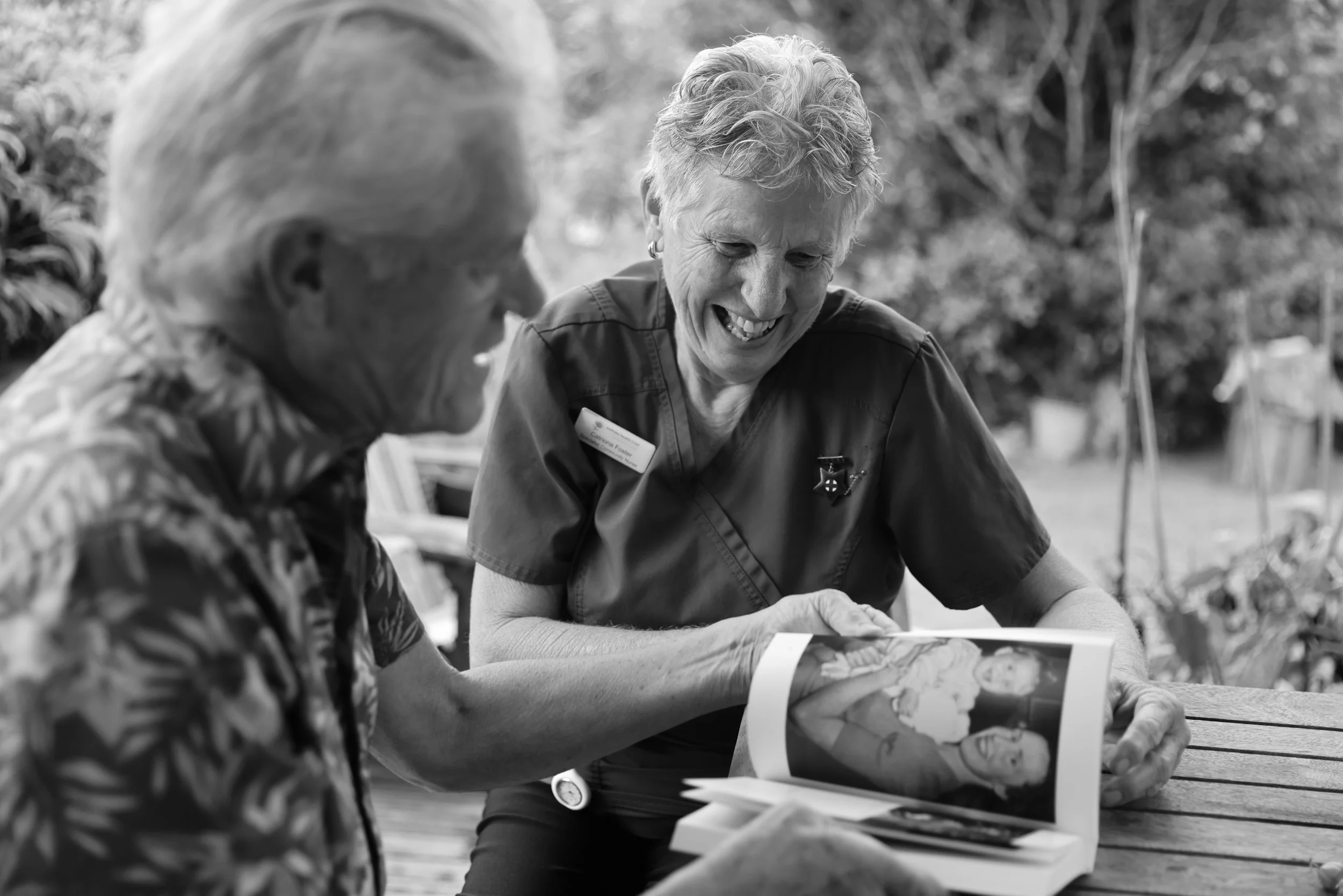 An in-home specialist nurse sits beside a family member, gently turning the pages of a photo album together.