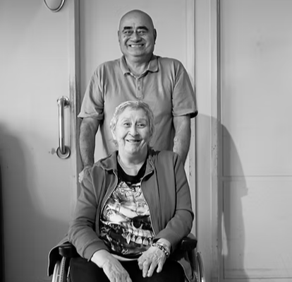 A photo of a local Waiheke man standing behind his wife in a wheelchair.