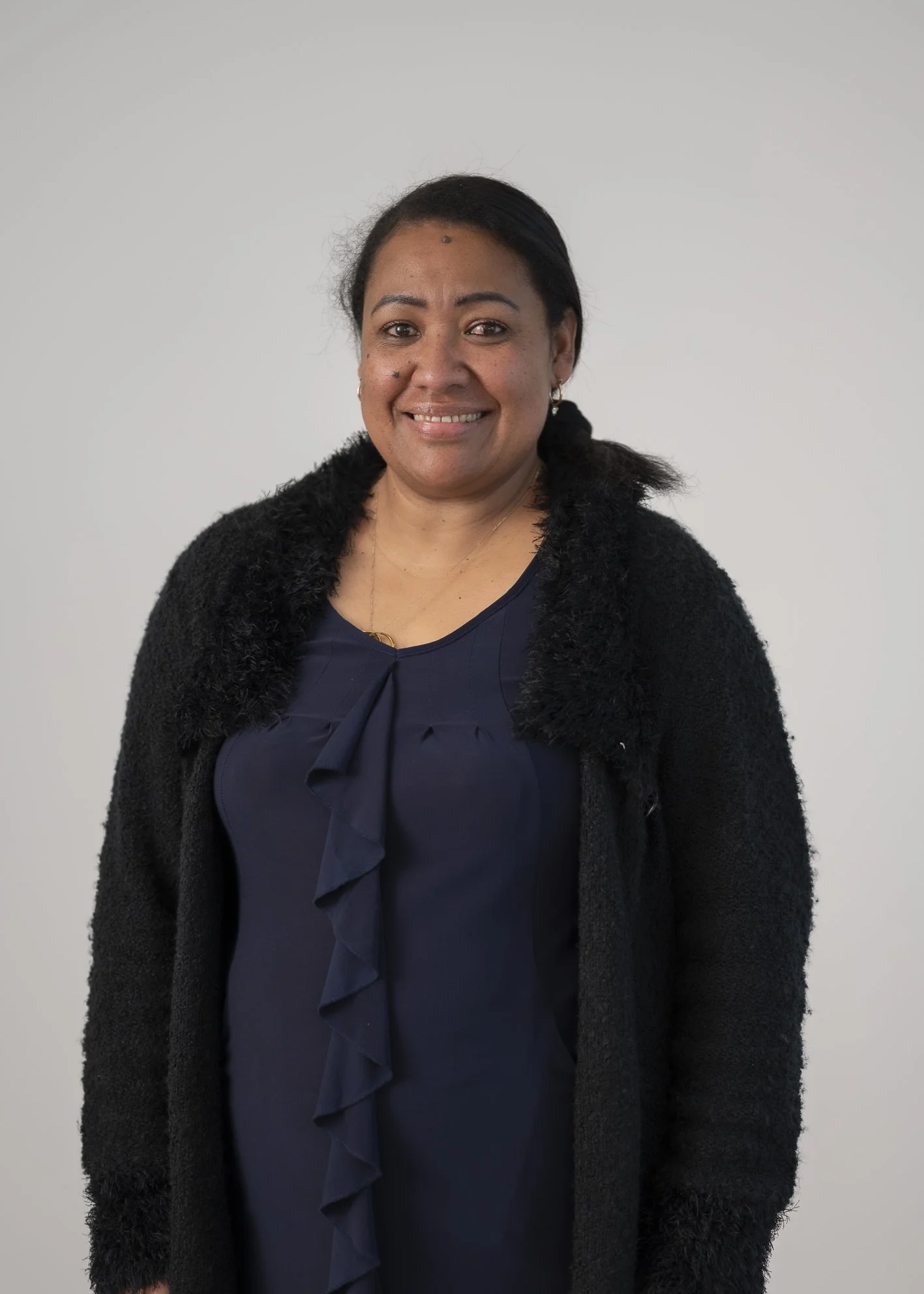 A portrait of a woman with dark hair, wearing a black cardigan and a navy blouse, smiling against a plain light gray background.