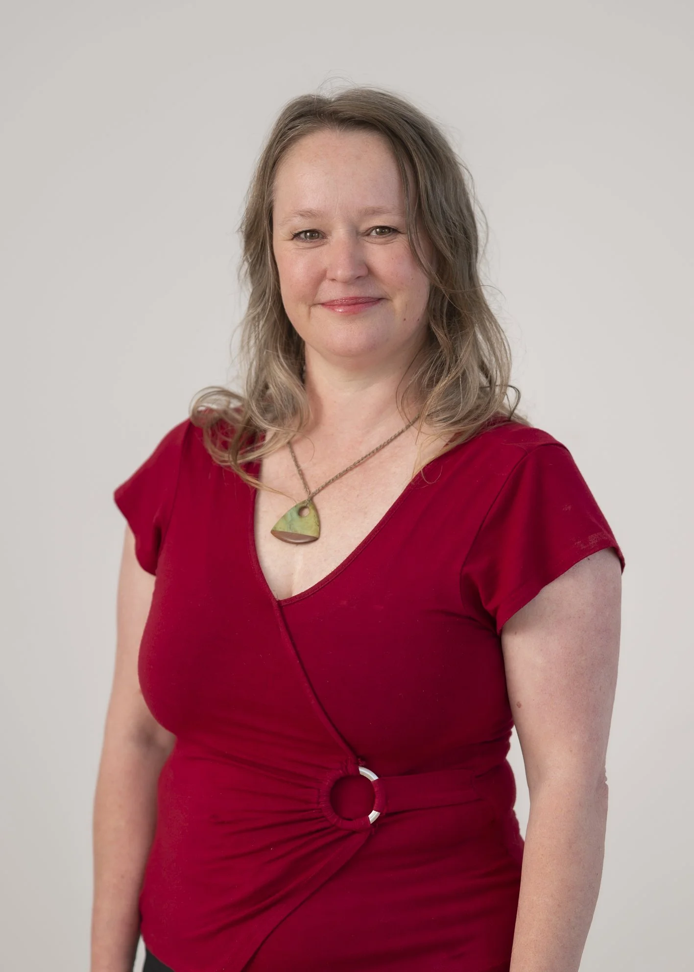 Portrait of Dr Stephanie Cox, Community Services Coordinator and Occupational Therapist, smiling in a red dress against a neutral background.