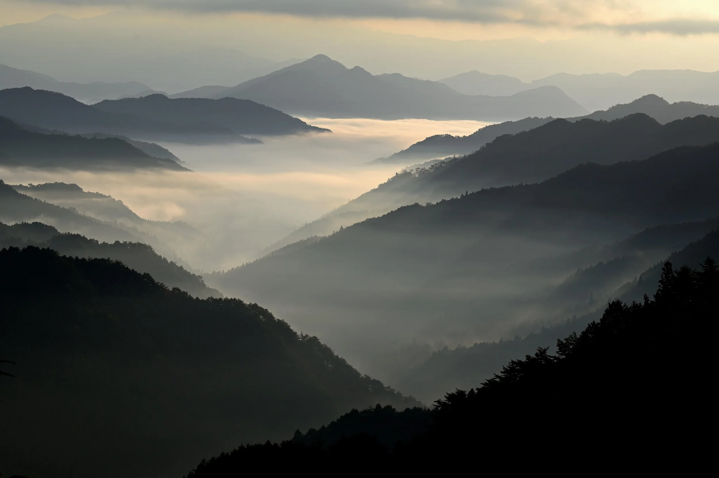 A scenic view of misty mountain peaks with layered ridges fading into the distance under a cloudy sky.