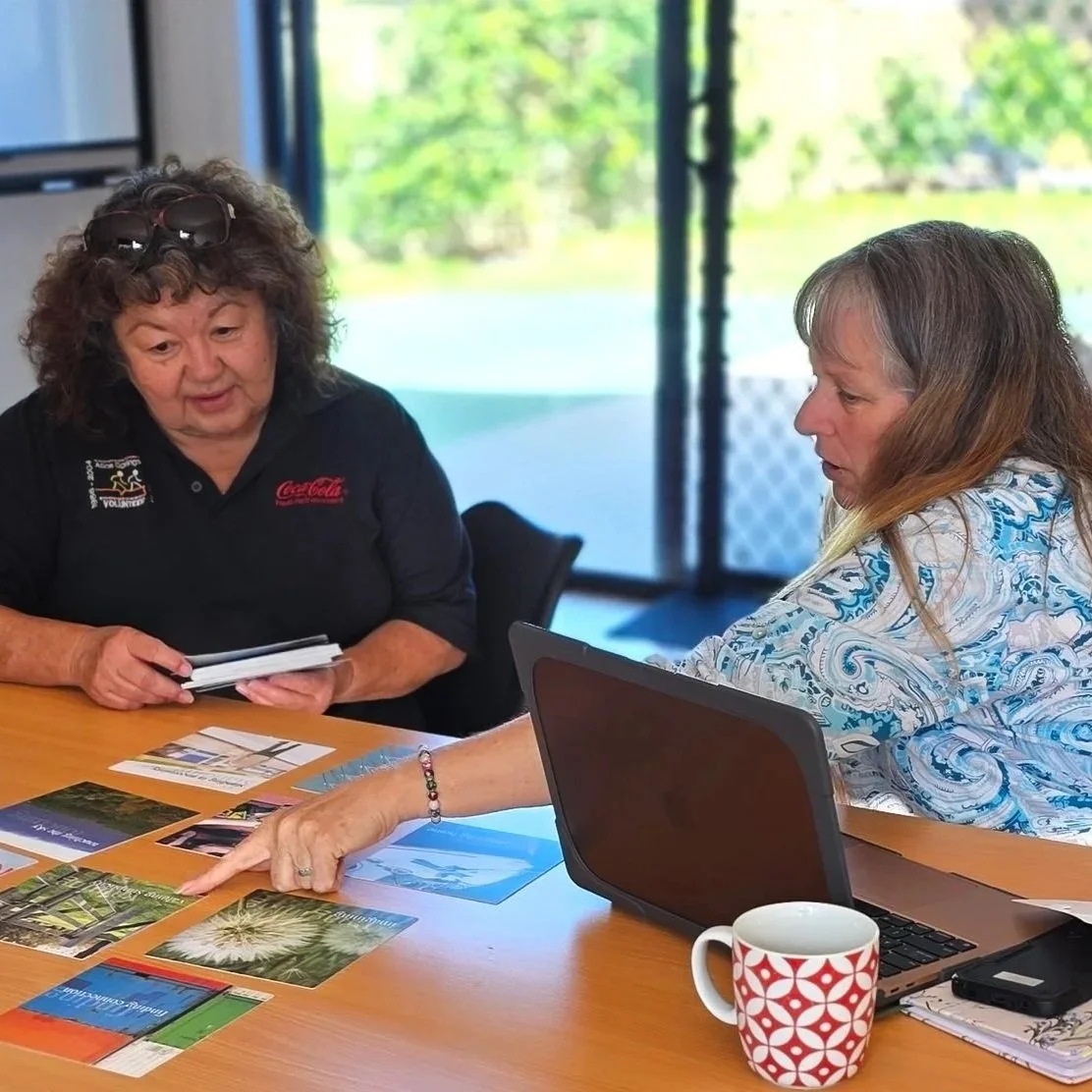 Two women sitting at a table discussing photos and documents, with a laptop.